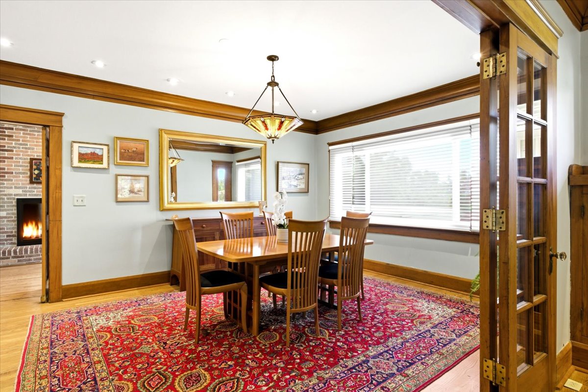 Formal dining area featuring hardwood flooring, extensive wood trim, a wide window with blinds, and a traditional chandelier