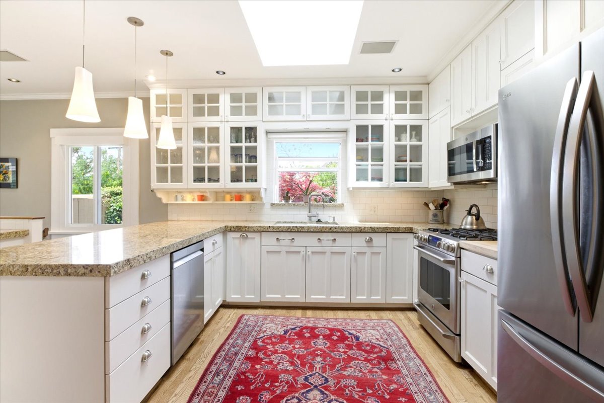 Kitchen featuring white cabinetry with glass-front uppers, granite countertops, stainless steel appliances, wood-finish flooring, and a large skylight