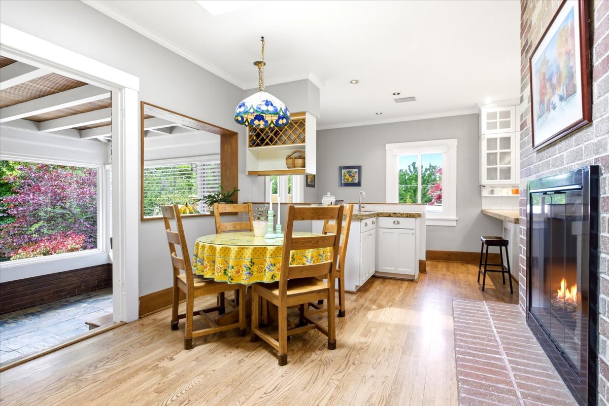 Open-concept dining area featuring wood-finish flooring, a brick fireplace, white cabinetry, a built-in wine rack, and direct access to an enclosed patio