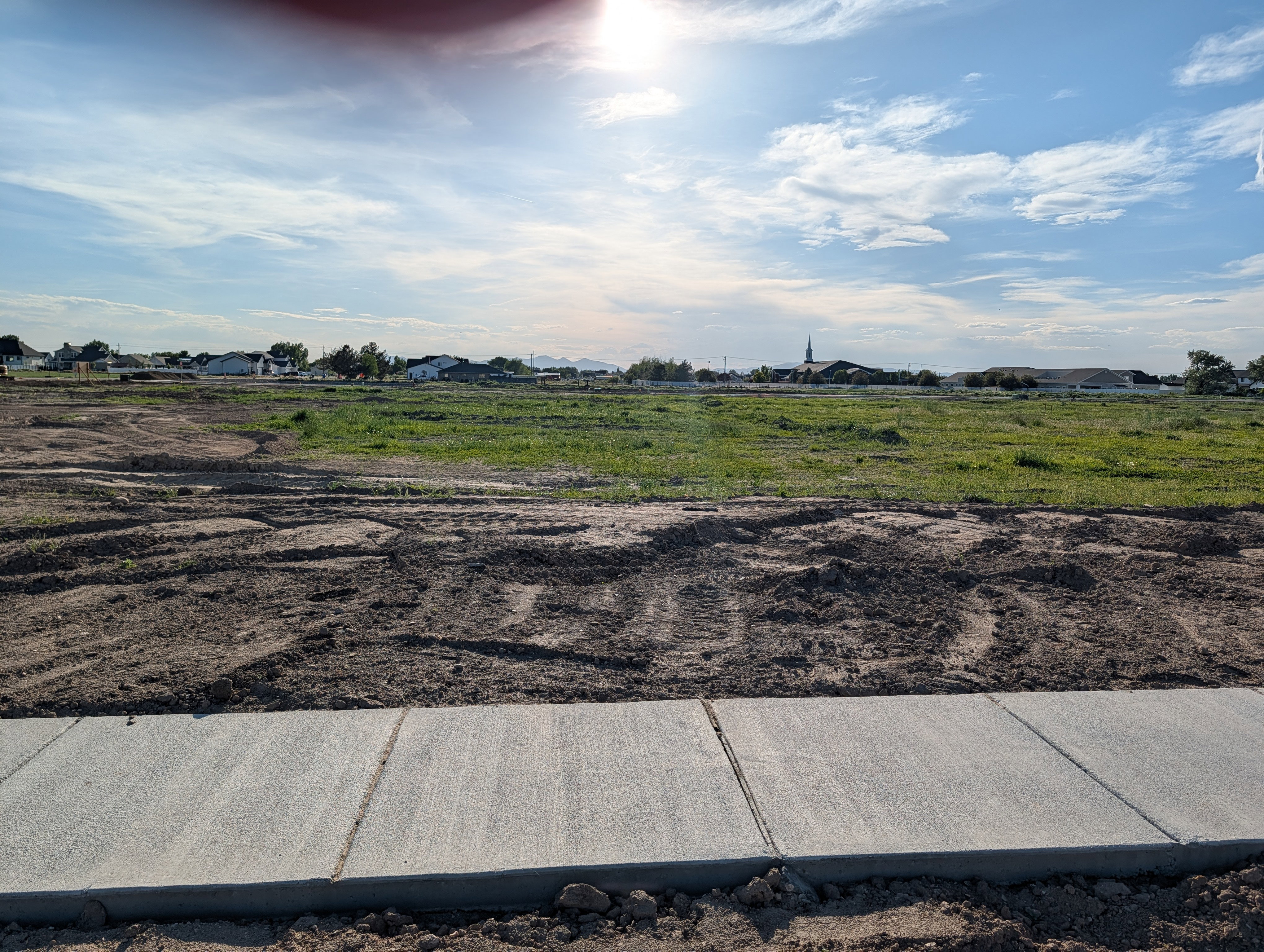 Expansive land parcel featuring a new concrete sidewalk, graded earth, and existing green spaces