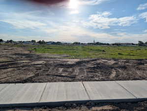 Expansive land parcel featuring a new concrete sidewalk, graded earth, and existing green spaces