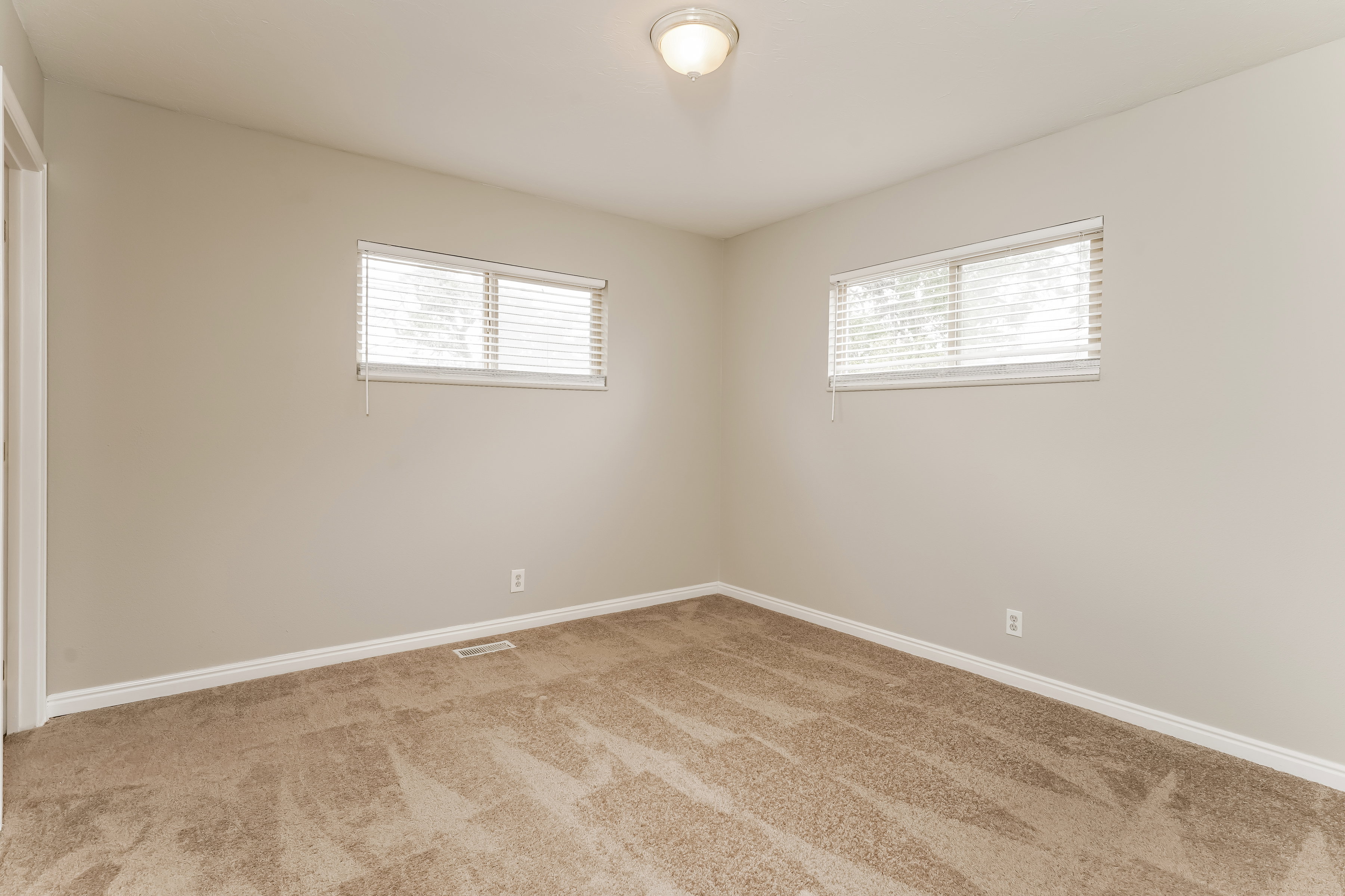 Neutral tone wall paint with white trim, tan carpet flooring, and two windows featuring blinds