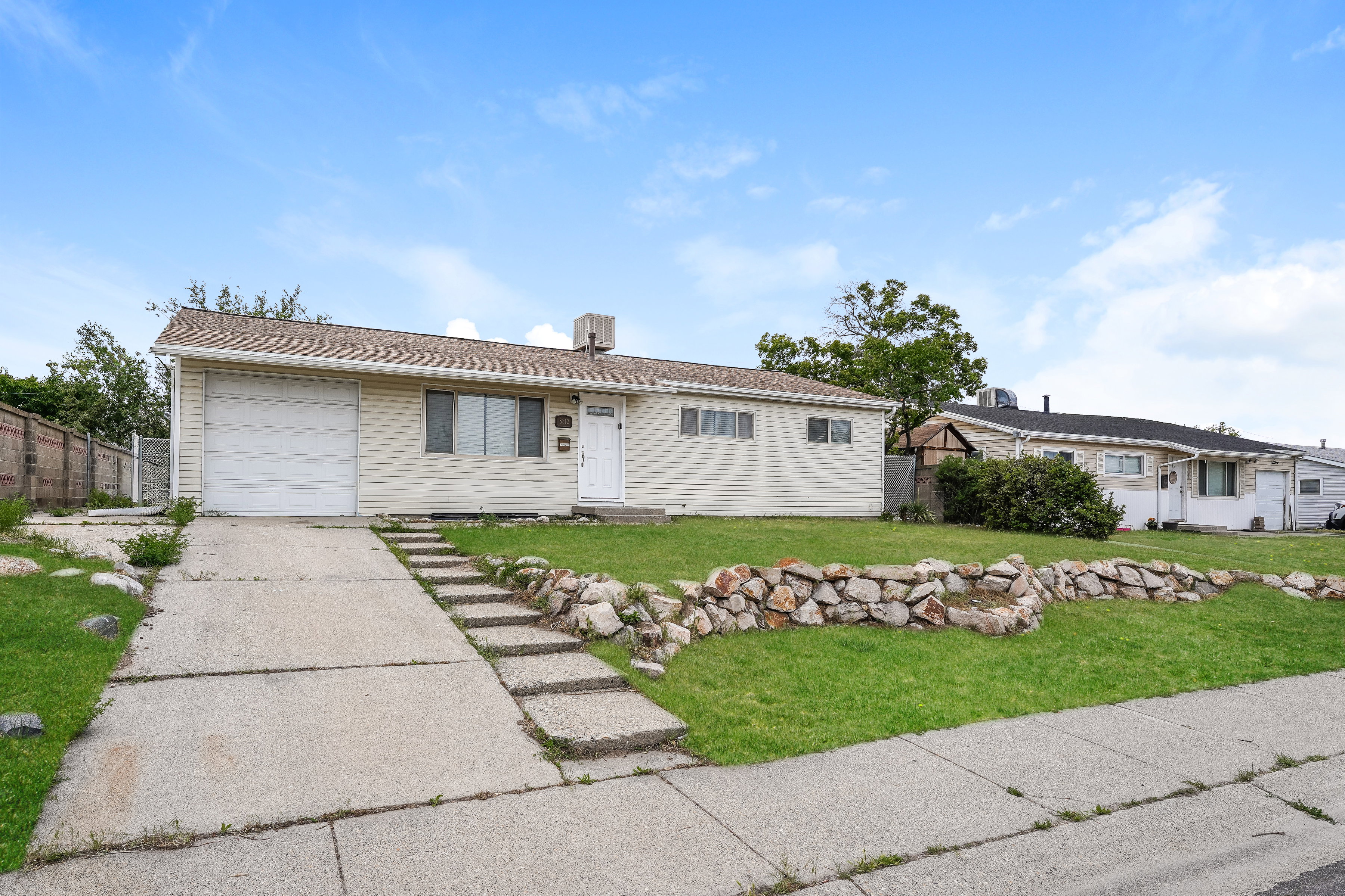 Ranch-style residence featuring light-colored siding, an attached garage, and a front entry door