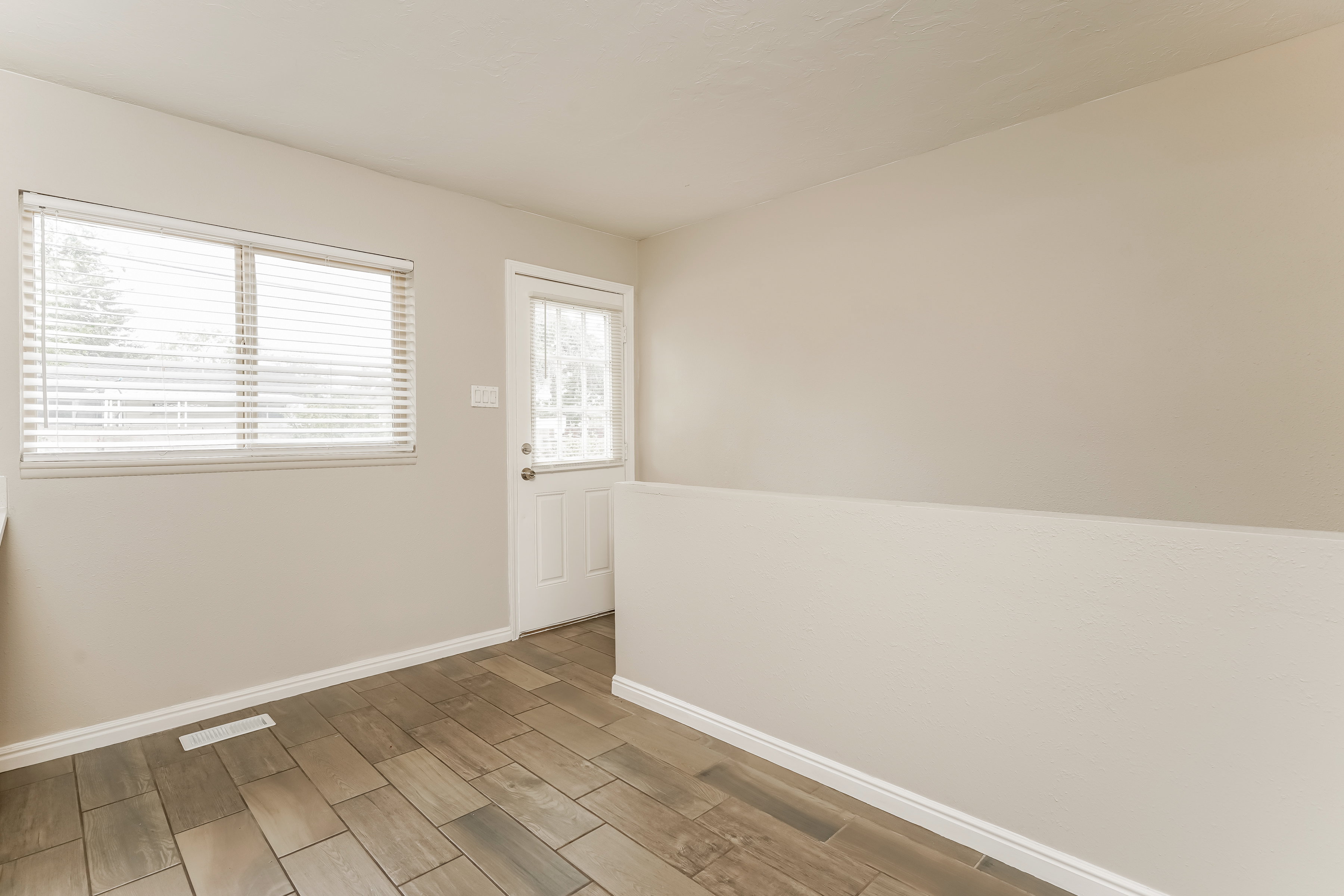 Neutral-toned interior featuring wood-finish tile flooring, a window with blinds, and a white paneled door with a glass insert