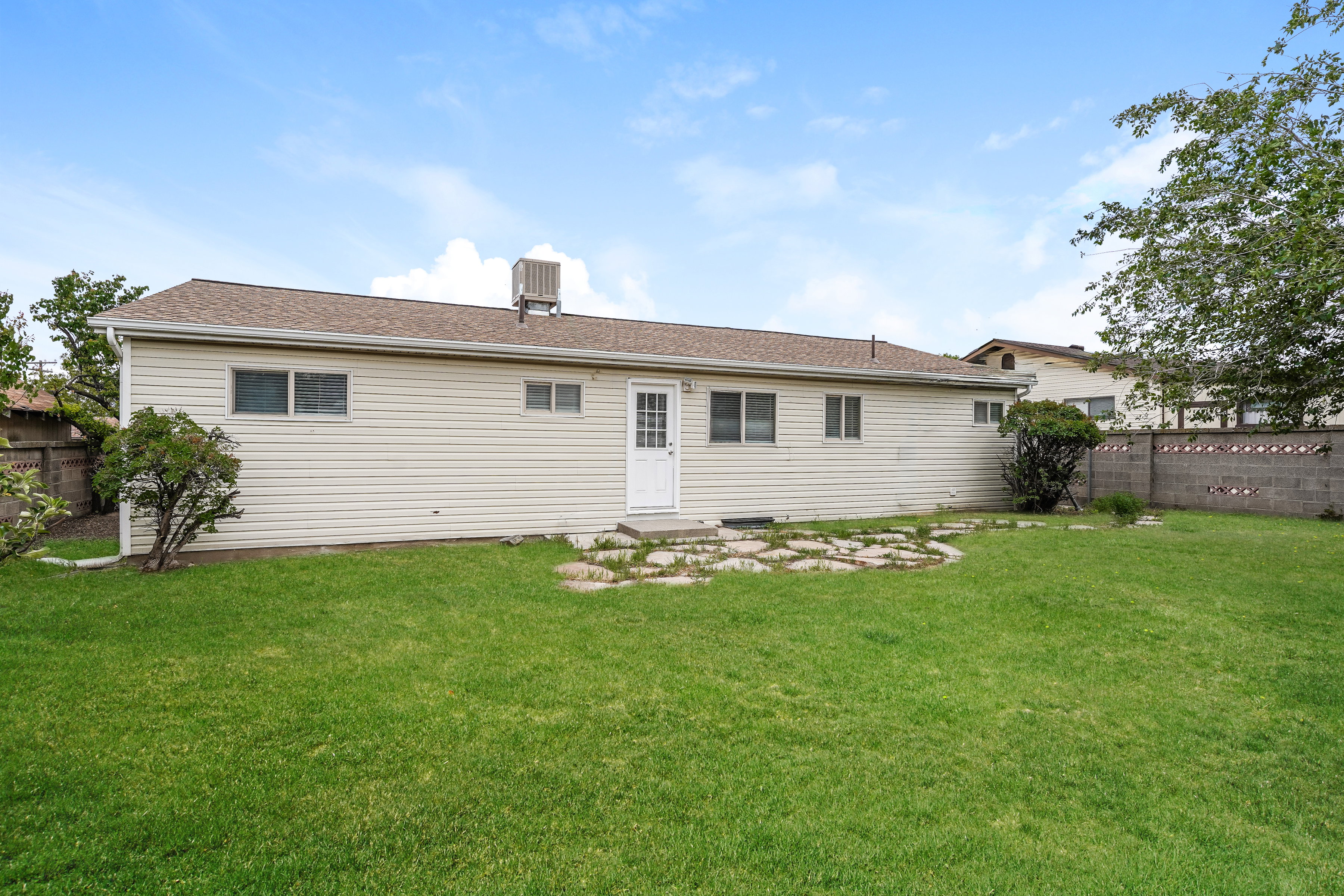 Expansive backyard featuring a lush lawn, stone pathway, rear exterior access door, and a privacy wall