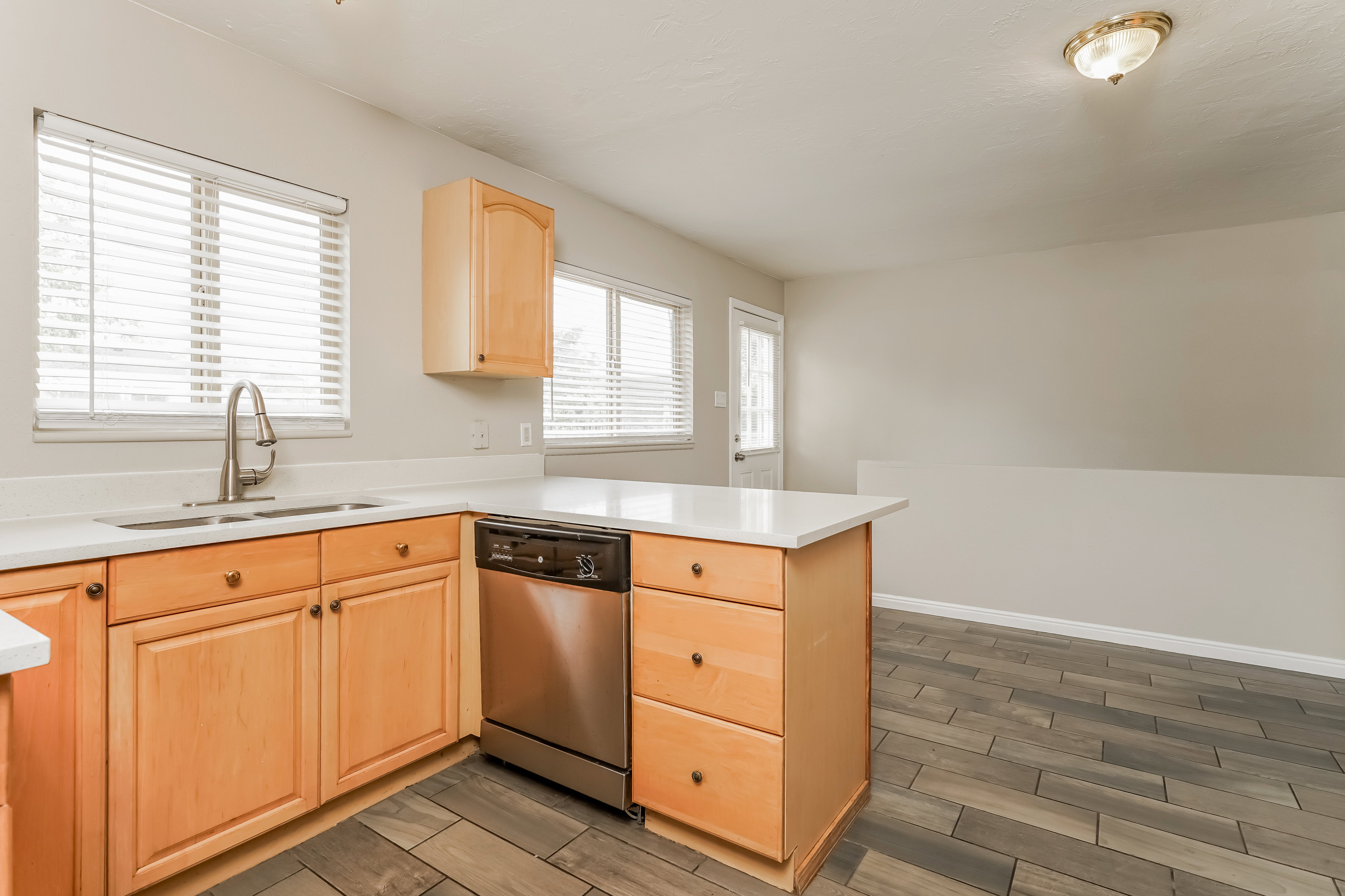Kitchen featuring wood cabinetry, stainless steel dishwasher, dual basin sink with gooseneck faucet, light-toned countertops, and tile flooring