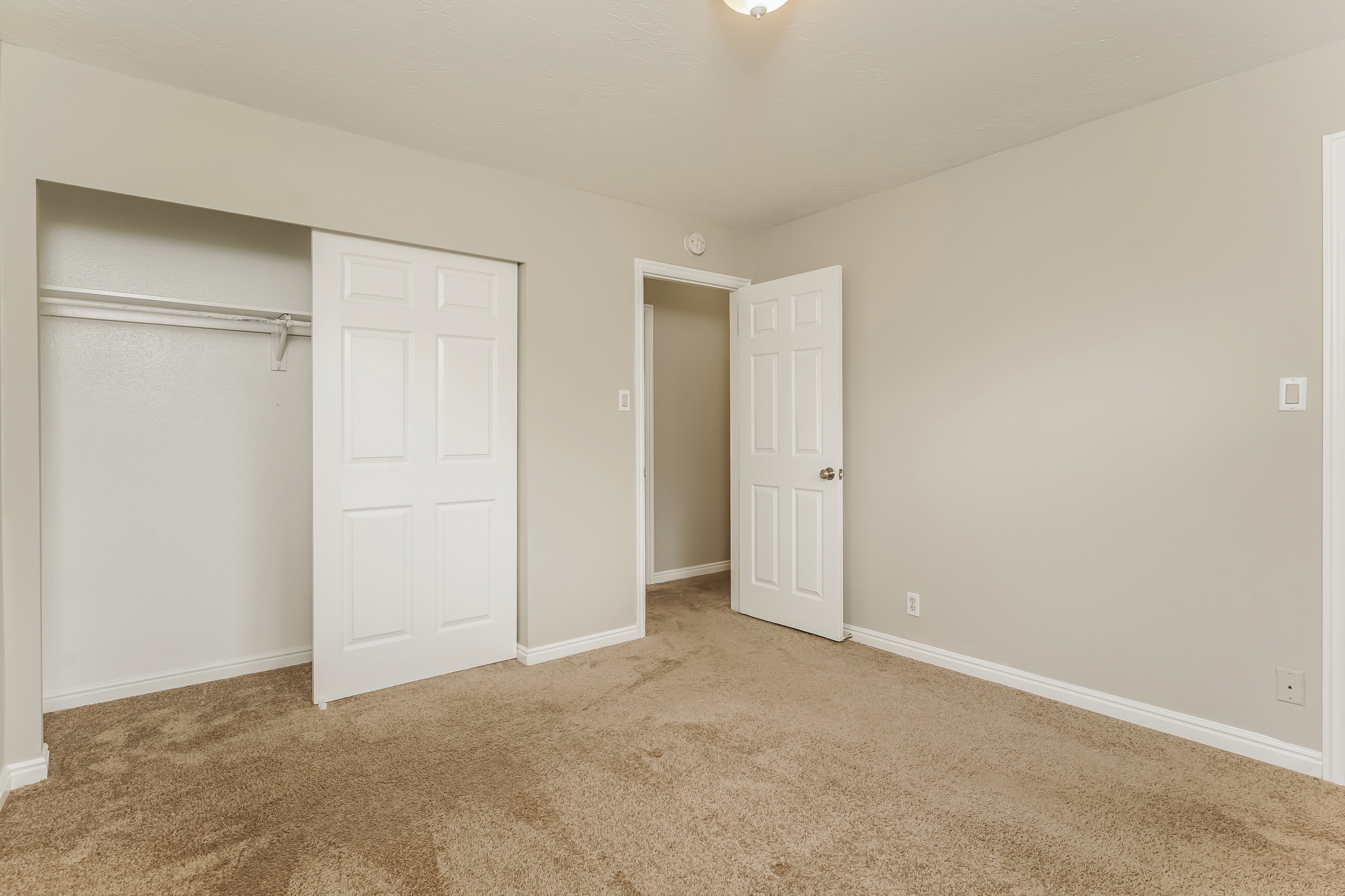 Bedroom featuring neutral carpeting, a closet with sliding panel doors, and a ceiling-mounted light fixture