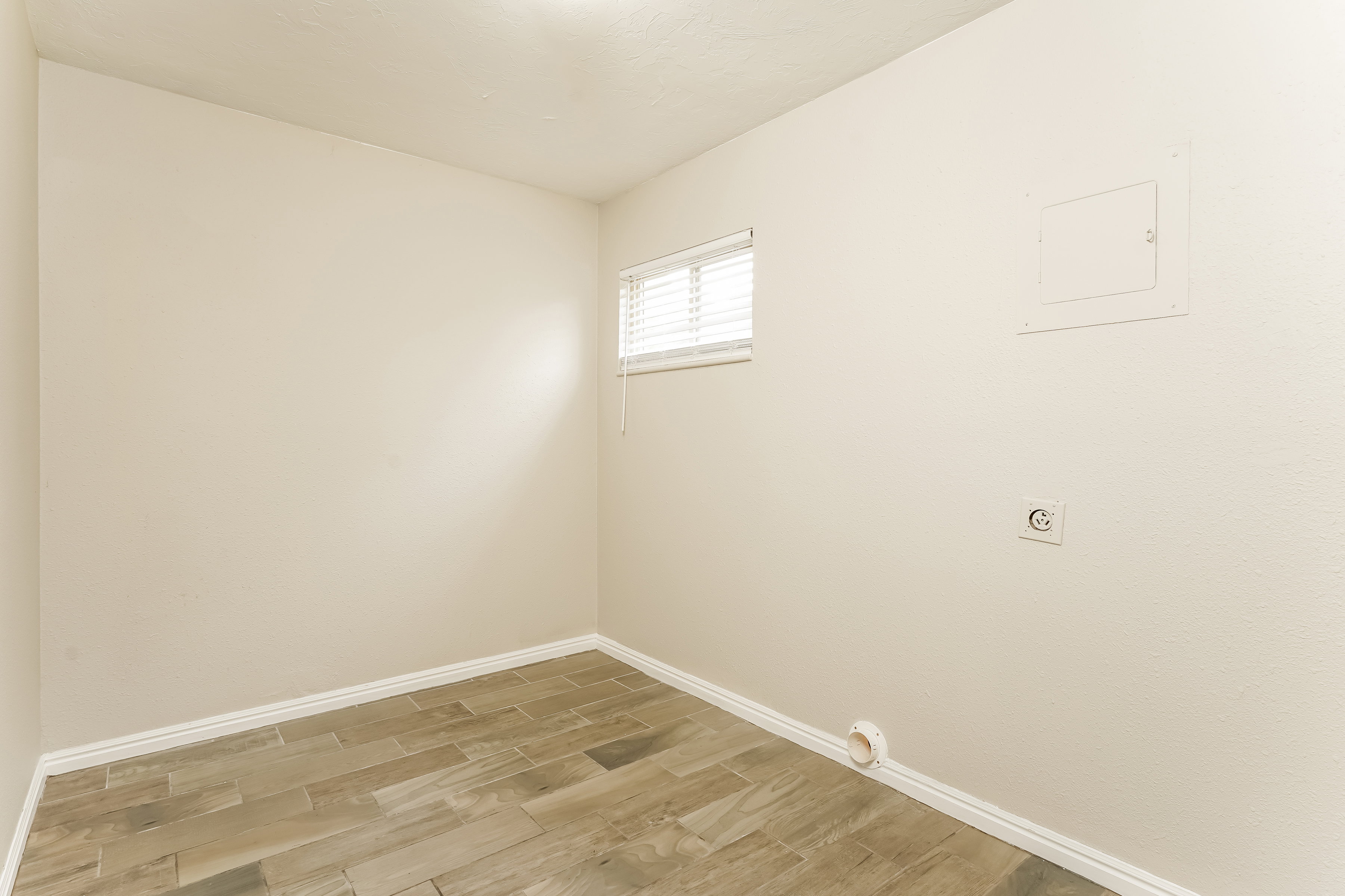Utility space featuring wood-finish flooring, a window with blinds, and white baseboards