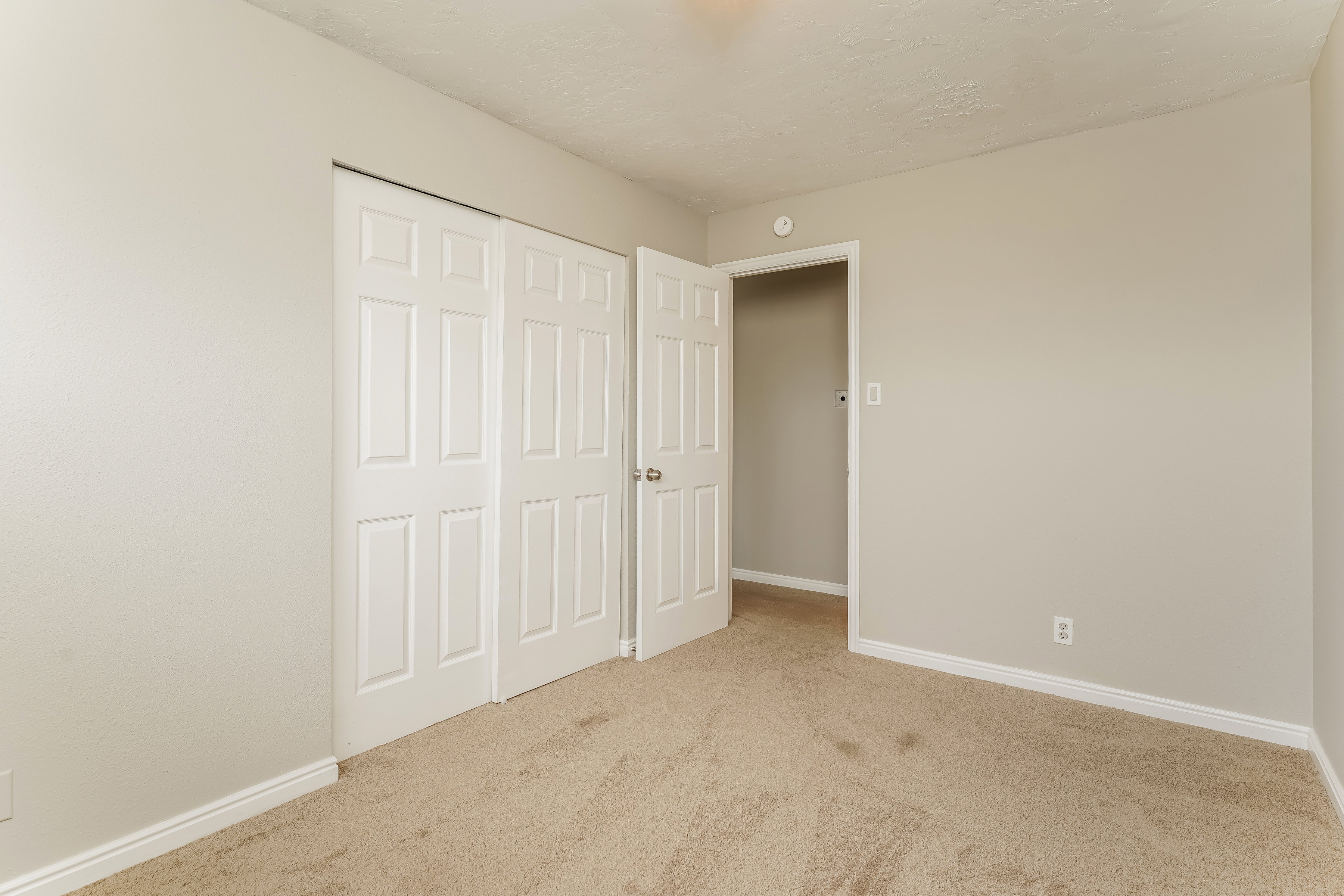Neutral-toned room featuring light beige carpeting, white baseboards, and a pair of white bi-fold closet doors