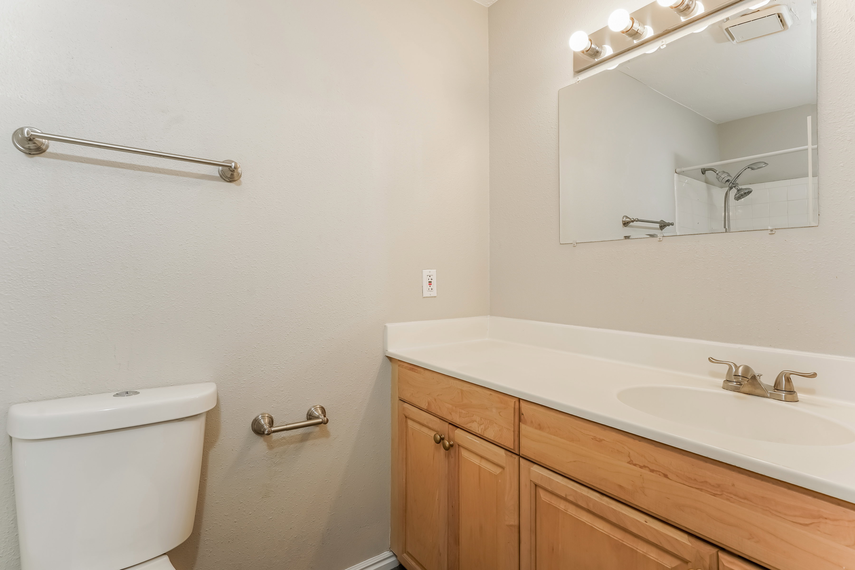 Bathroom featuring a light-toned vanity with an integrated sink, a large wall-mounted mirror, and a three-light fixture