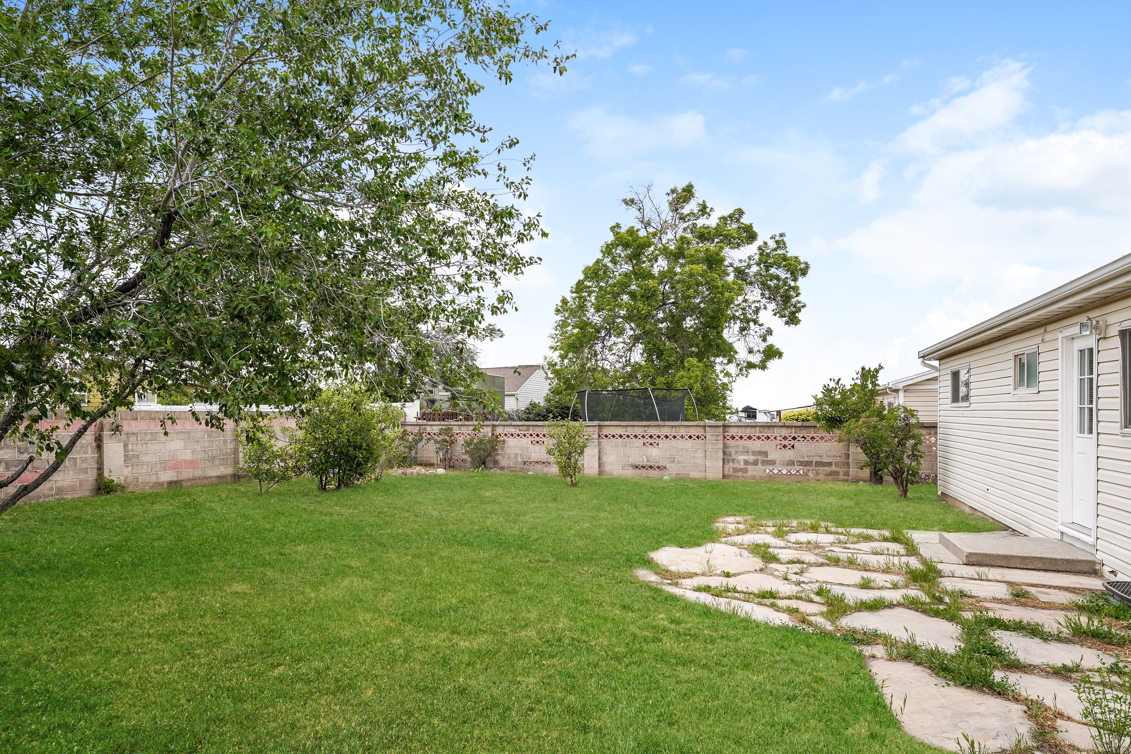Expansive green lawn with mature trees and perimeter block wall