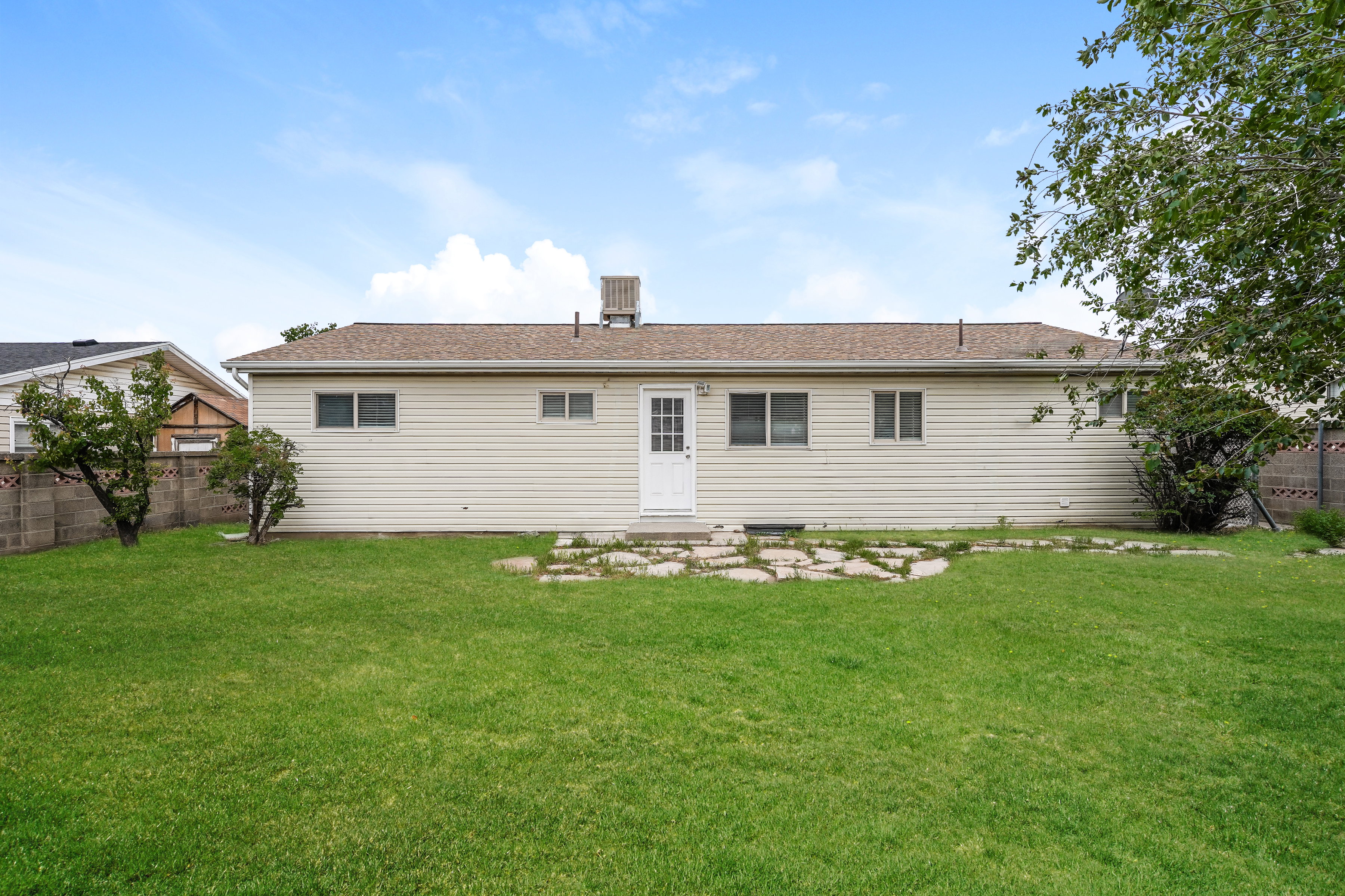 Expansive backyard featuring a large green lawn, concrete block perimeter fencing, and a stone paver patio area