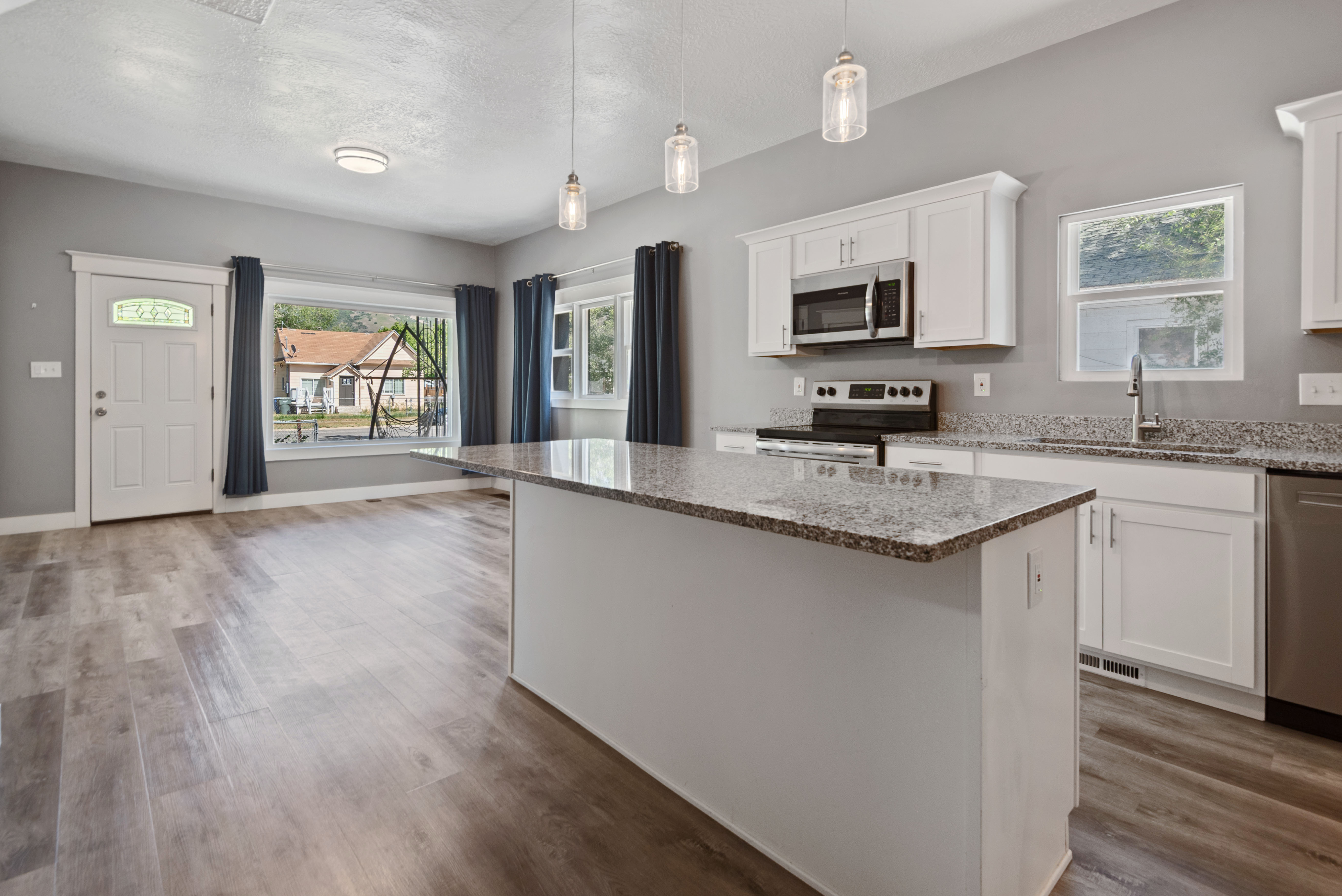 Open-concept living area featuring wood-finish flooring, white cabinetry, granite countertops, and stainless steel appliances