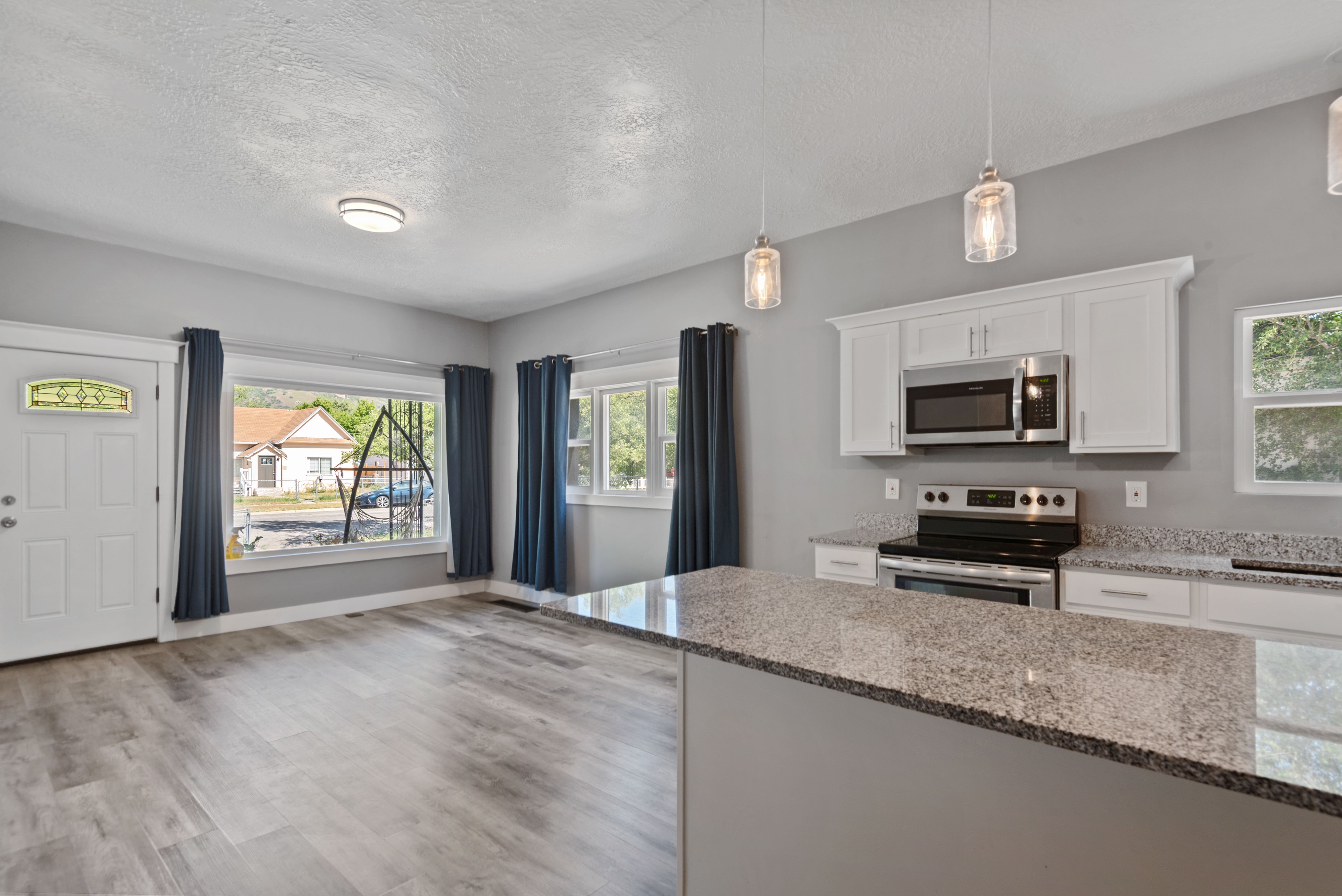 Open-concept living space featuring wood-finish flooring, a white paneled entry door with decorative glass, and multiple windows for abundant natural light