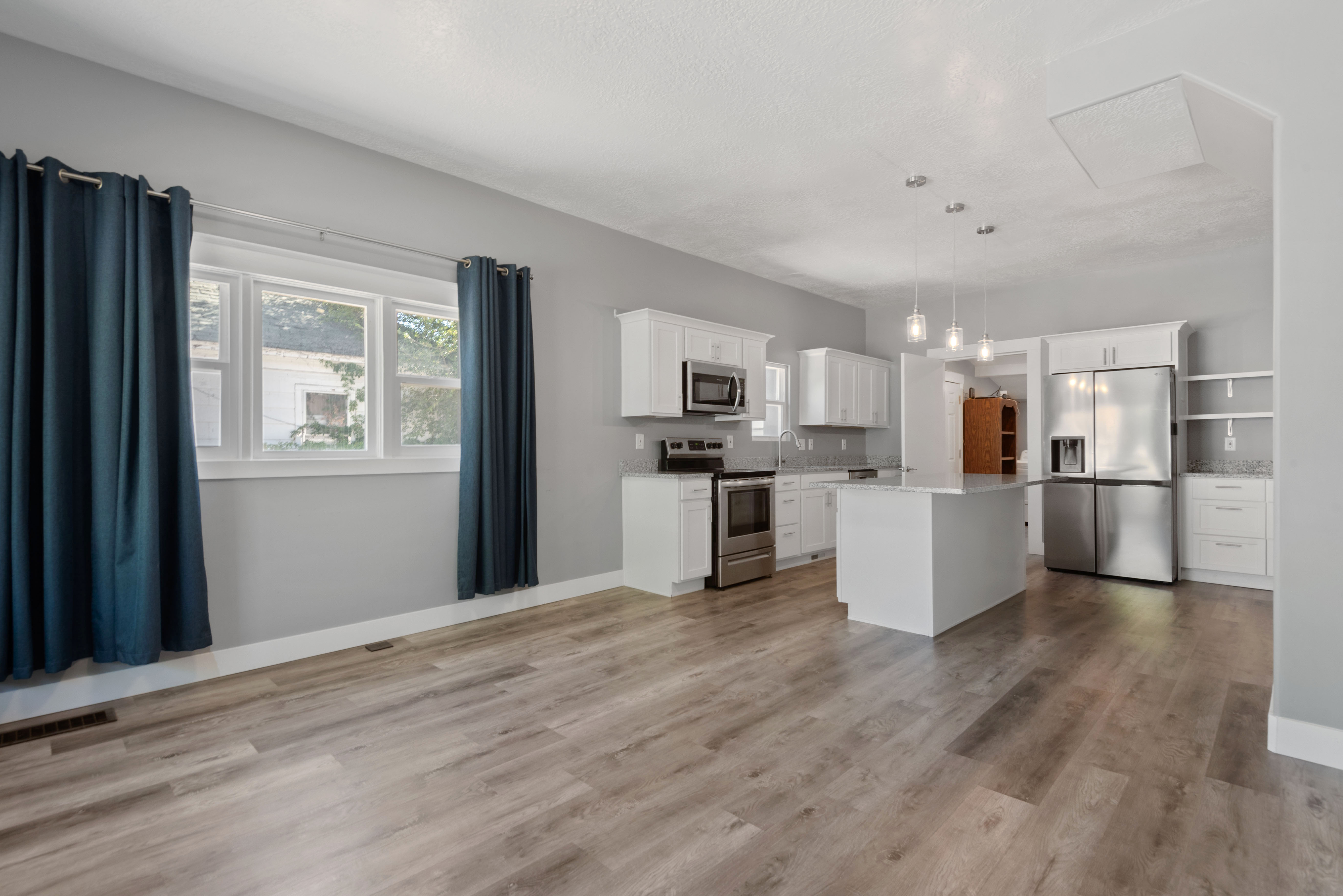 Open-concept living space featuring wood-finish flooring, a kitchen island, stainless steel appliances, white cabinetry, and recessed lighting