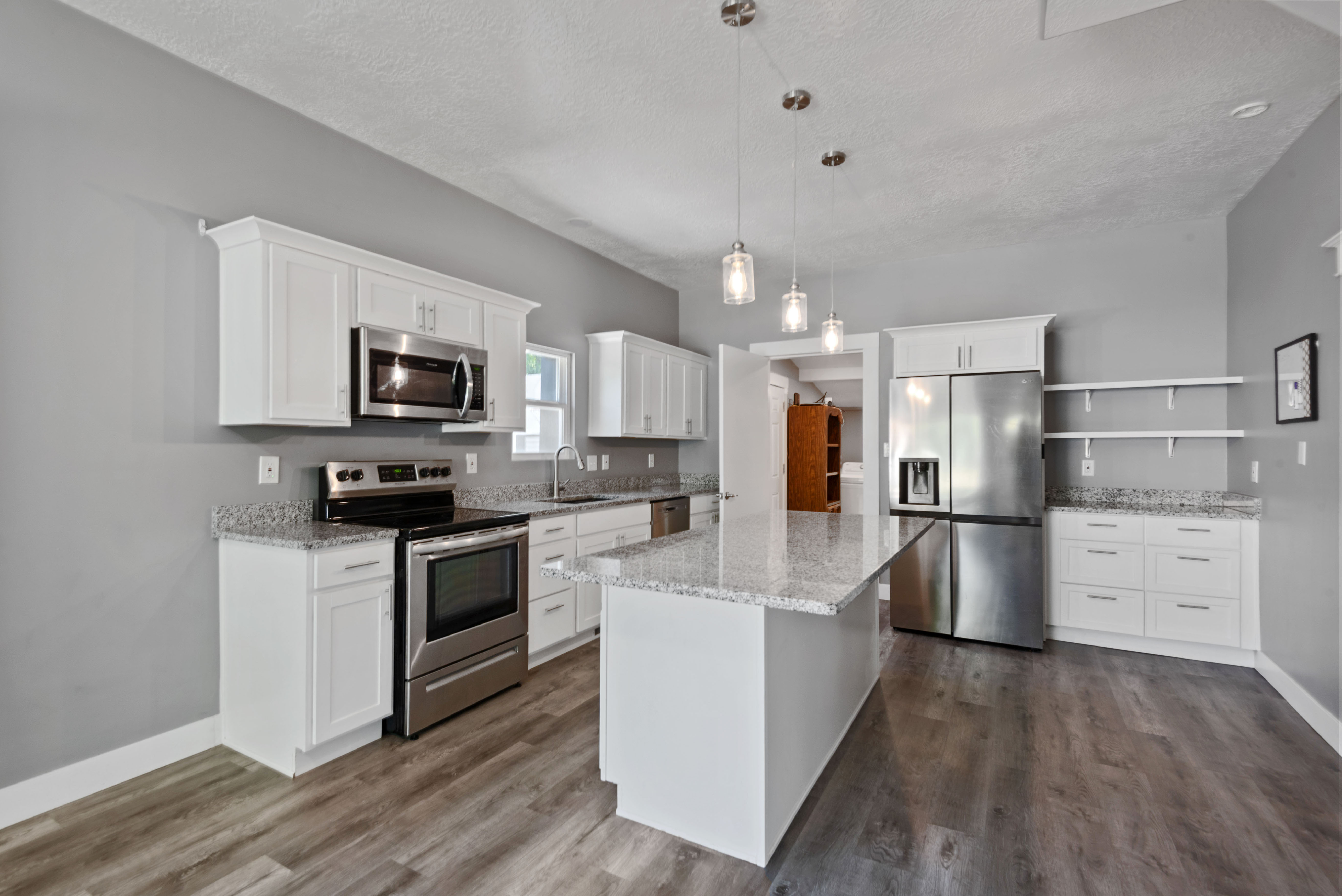 Modern kitchen featuring white cabinetry, light-toned countertops, stainless steel appliances, a center island with pendant lighting, and wood-finish flooring