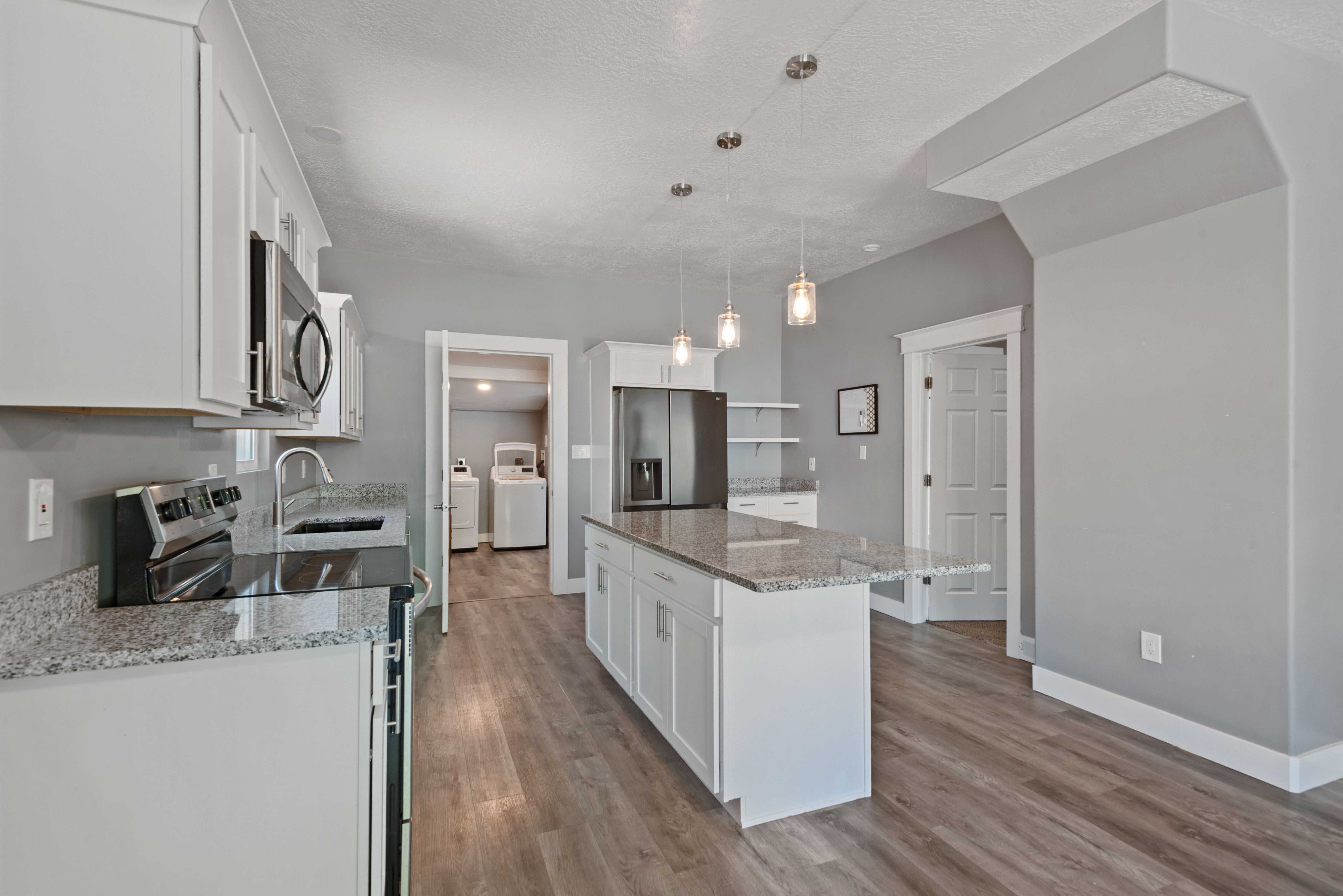 Open-concept kitchen featuring an island with granite-style countertops, stainless steel appliances, white cabinetry, and wood-finish flooring