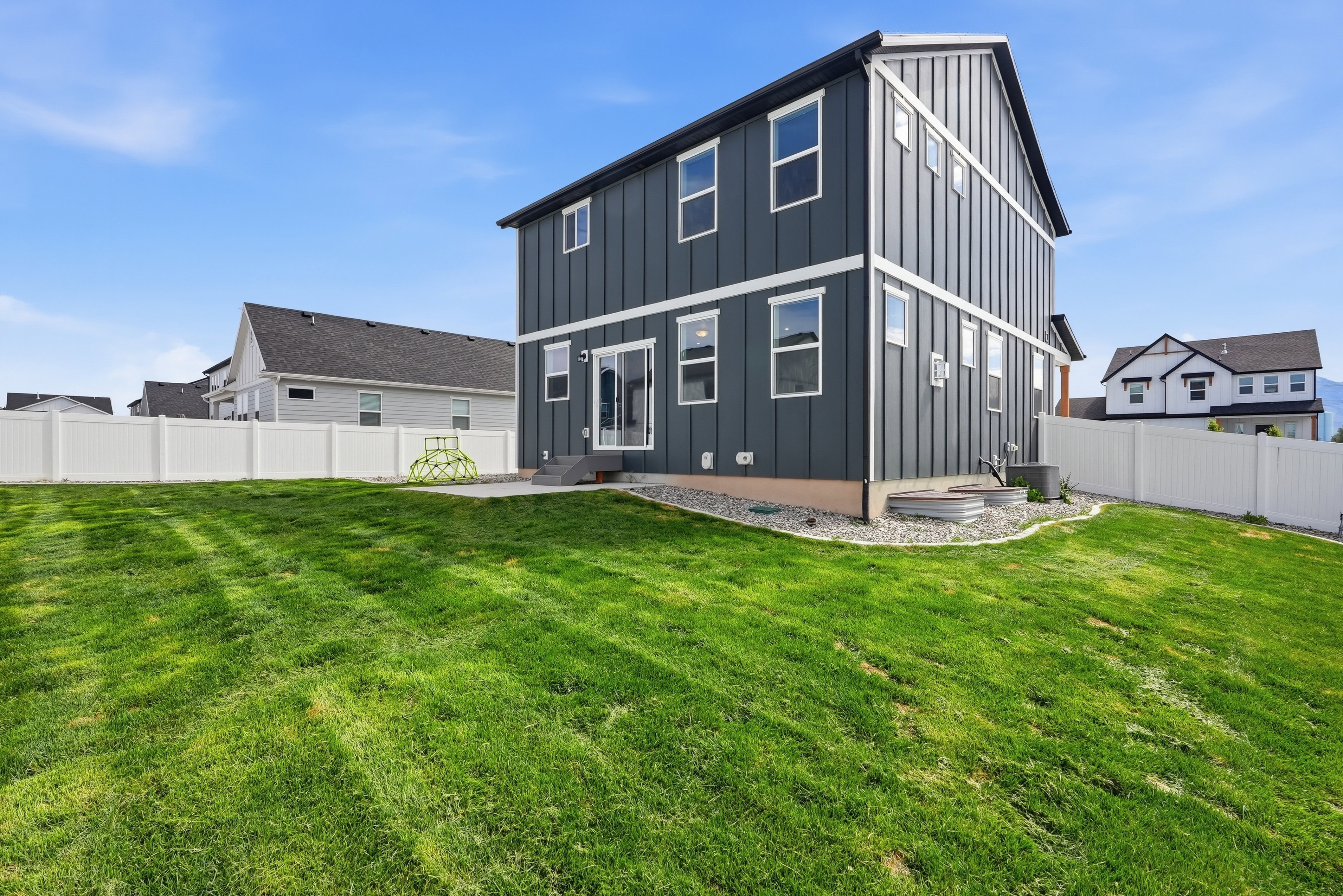 Spacious backyard featuring a manicured lawn, white vinyl fencing, and a concrete patio