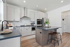 Contemporary kitchen featuring light wood-finish flooring, white cabinetry, dark countertops, and a subway tile backsplash