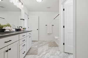 Bathroom featuring a dual vanity with a dark countertop and white cabinetry, marble-look floor tiling, a built-in bathtub with subway tile surround, and matte black fixtures