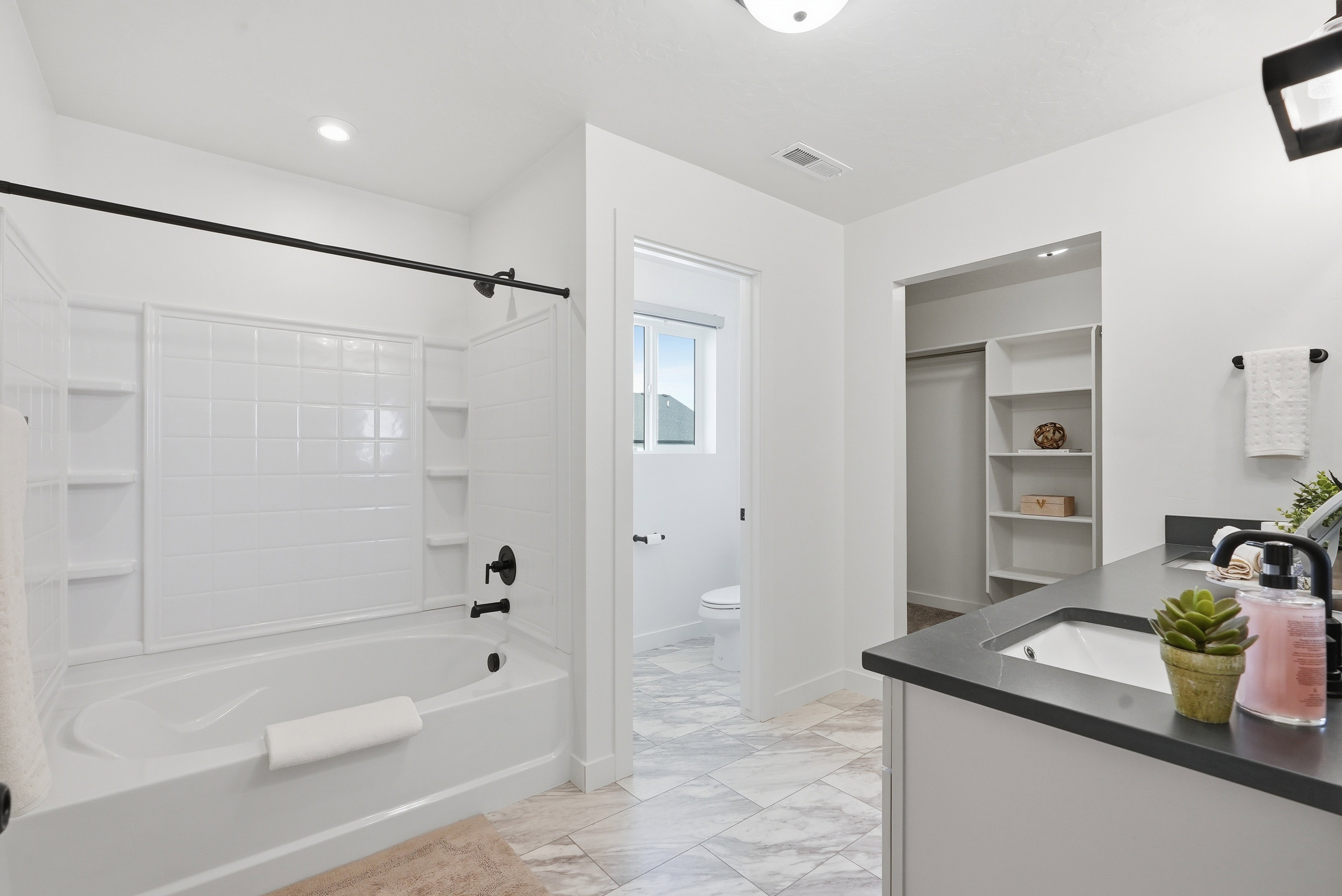 Modern bathroom featuring a white soaking tub with subway tile surround, black plumbing fixtures, and a dual-sink vanity with dark countertop