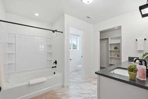 Modern bathroom featuring a white soaking tub with subway tile surround, black plumbing fixtures, and a dual-sink vanity with dark countertop