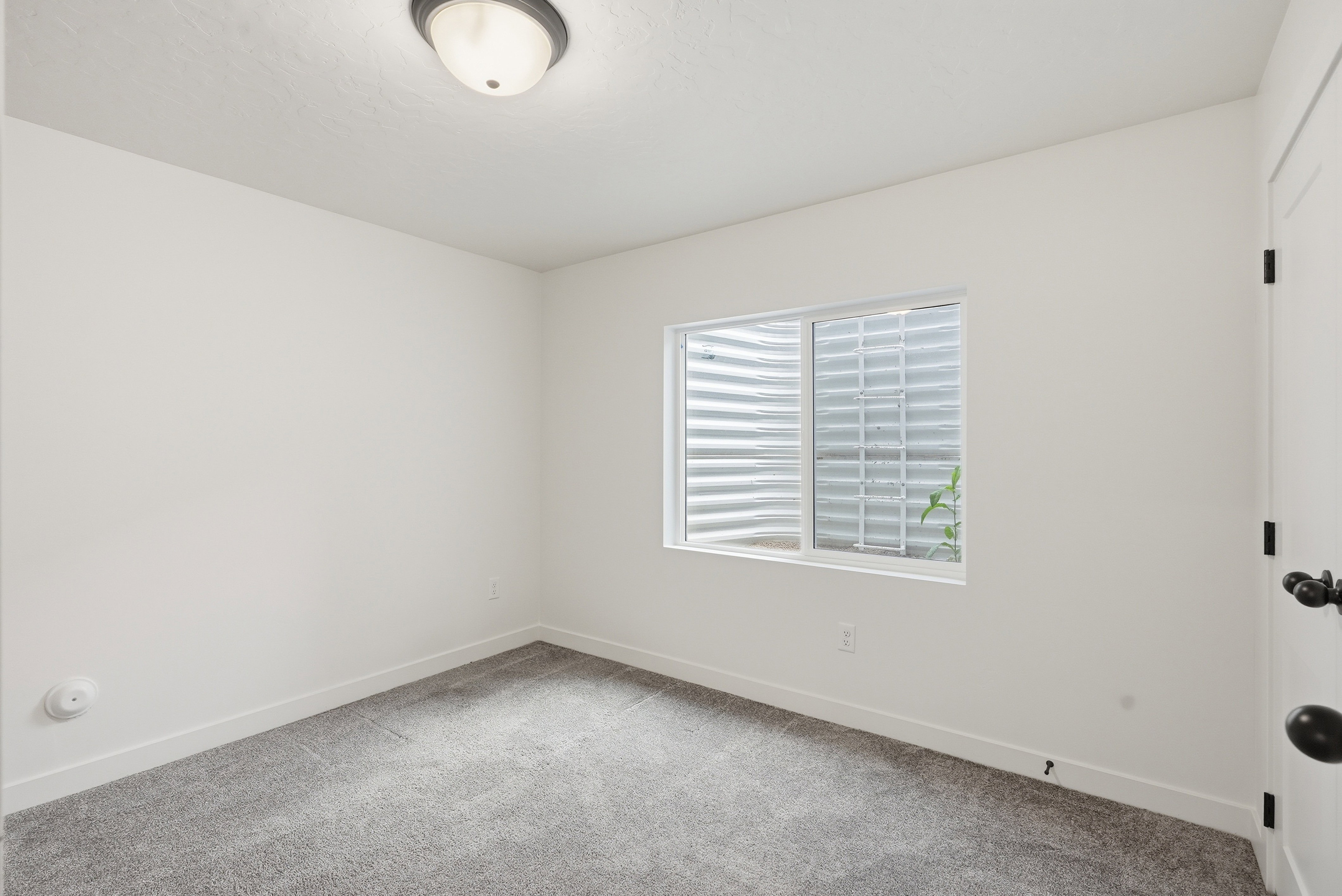 Carpeted room with a white door featuring matte black hardware, a window with a window well, and a flush mount ceiling light