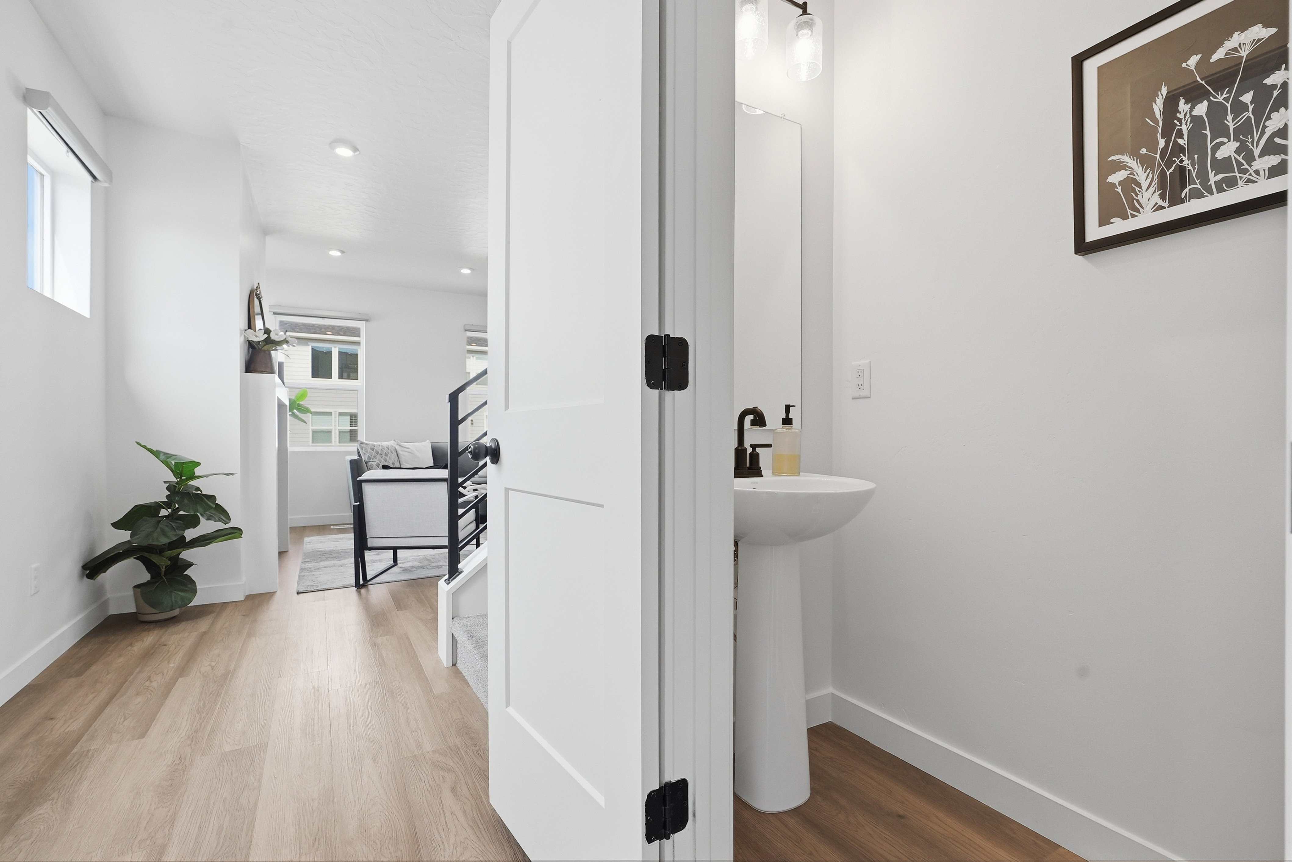 Powder room featuring a pedestal sink with a matte black faucet, mirrored vanity, and modern wall sconce