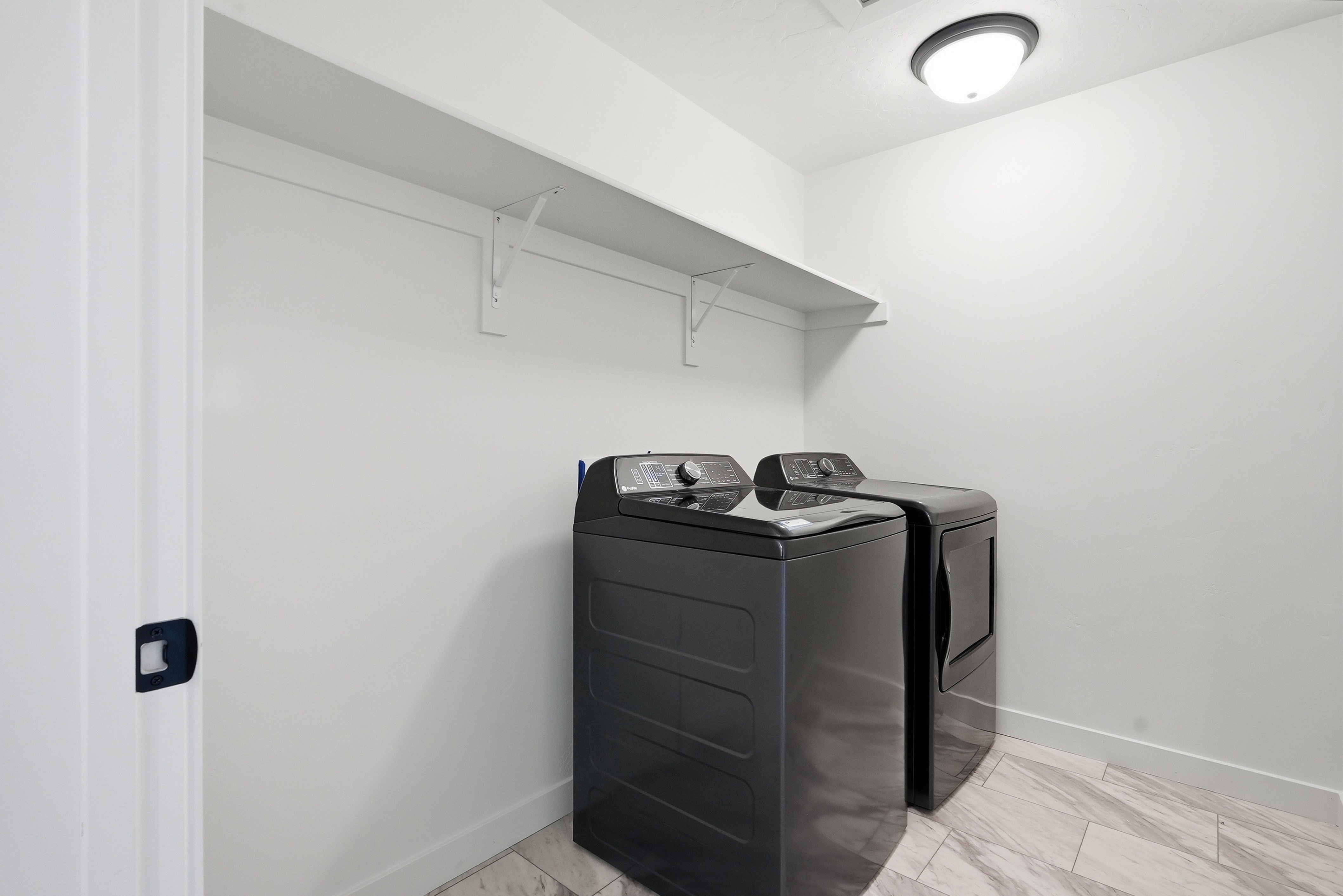 Laundry area featuring a ceiling-mounted light fixture, white walls, built-in shelving, and light-toned tile flooring