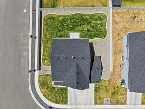 Aerial perspective highlighting a residential property with a dark shingled roof, a concrete driveway, and a front yard featuring a combination of gravel and lawn areas