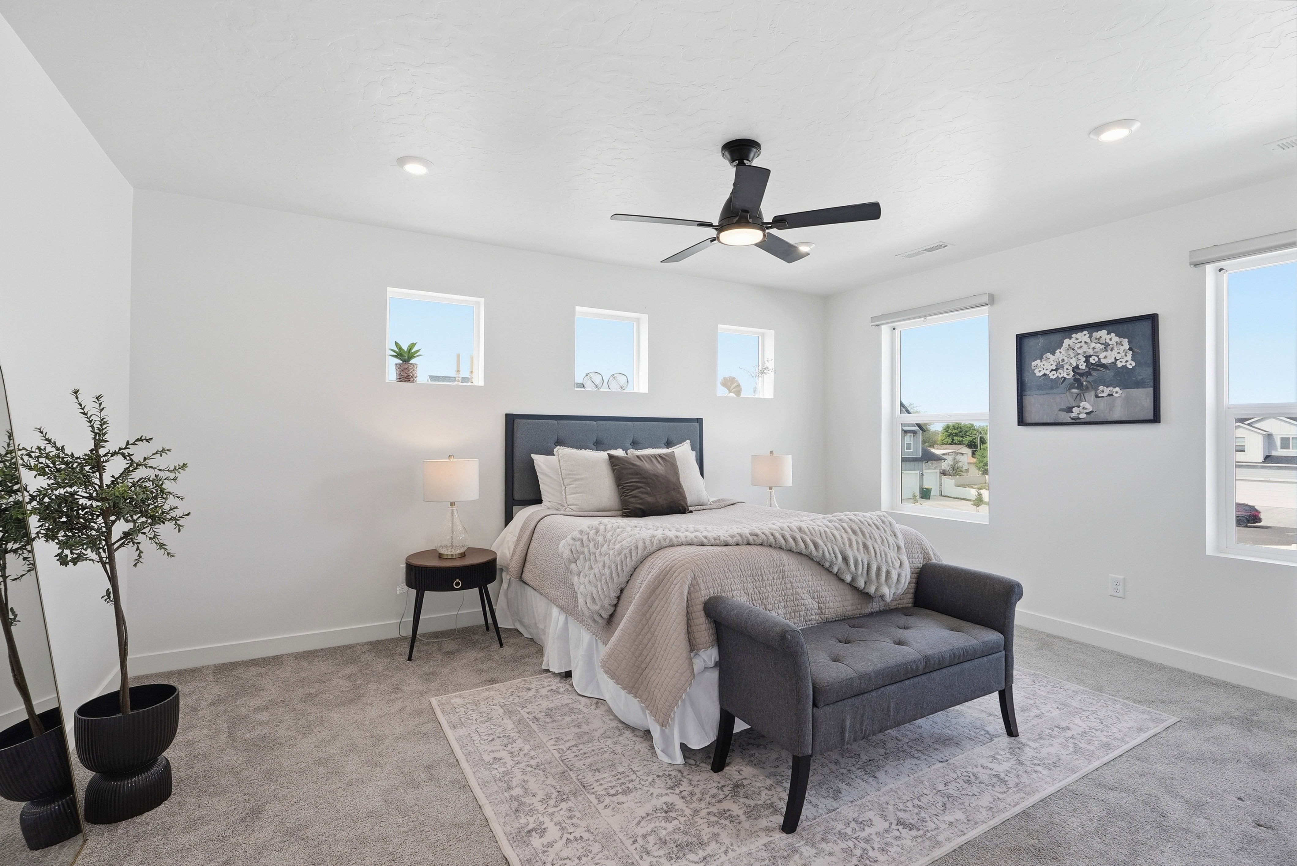 Spacious room featuring light gray carpet, white walls, multiple windows, a ceiling fan with light, and recessed lighting