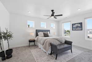 Spacious room featuring light gray carpet, white walls, multiple windows, a ceiling fan with light, and recessed lighting