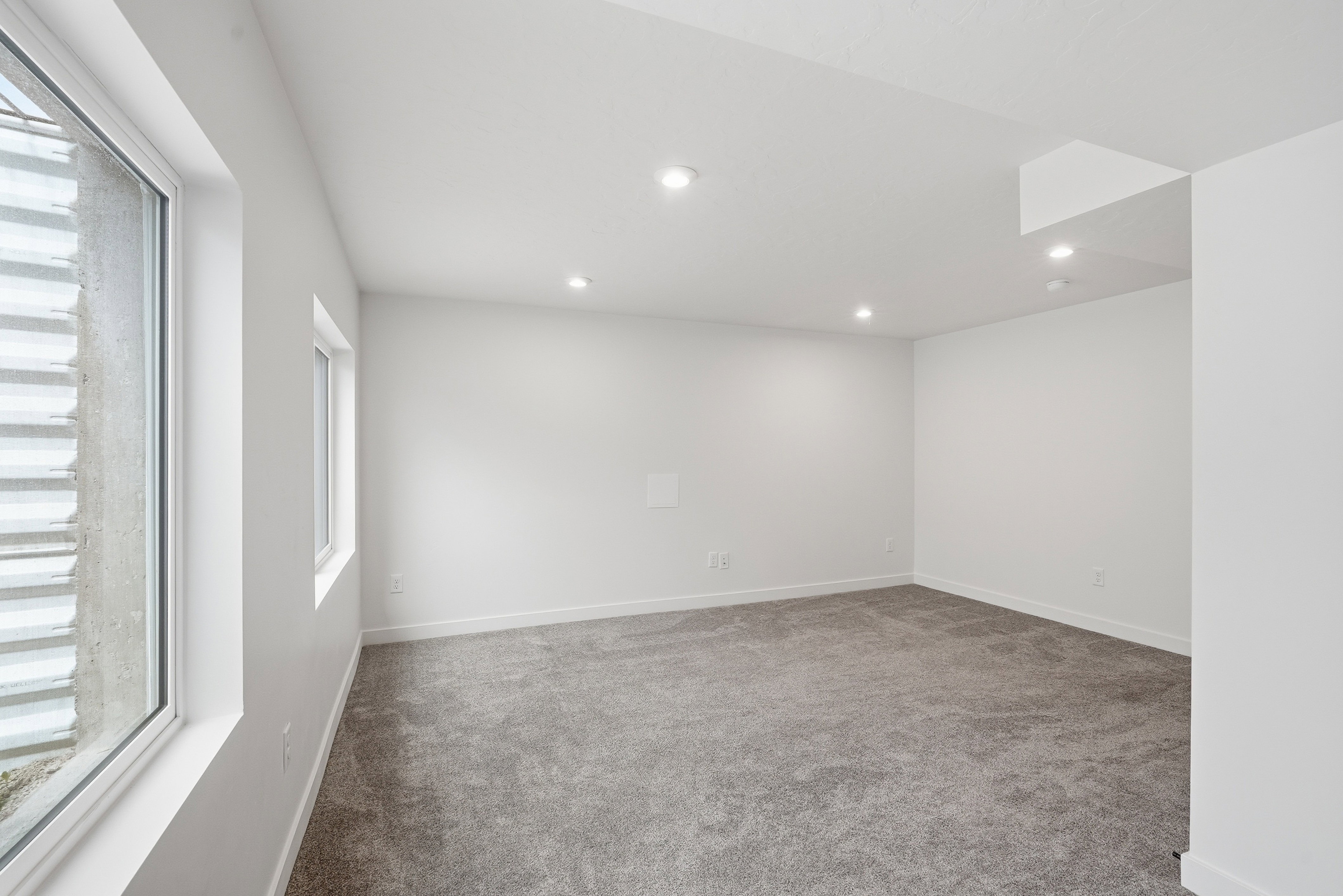 Spacious room featuring light gray carpet, recessed ceiling lighting, and white walls