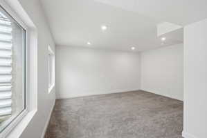 Spacious room featuring light gray carpet, recessed ceiling lighting, and white walls
