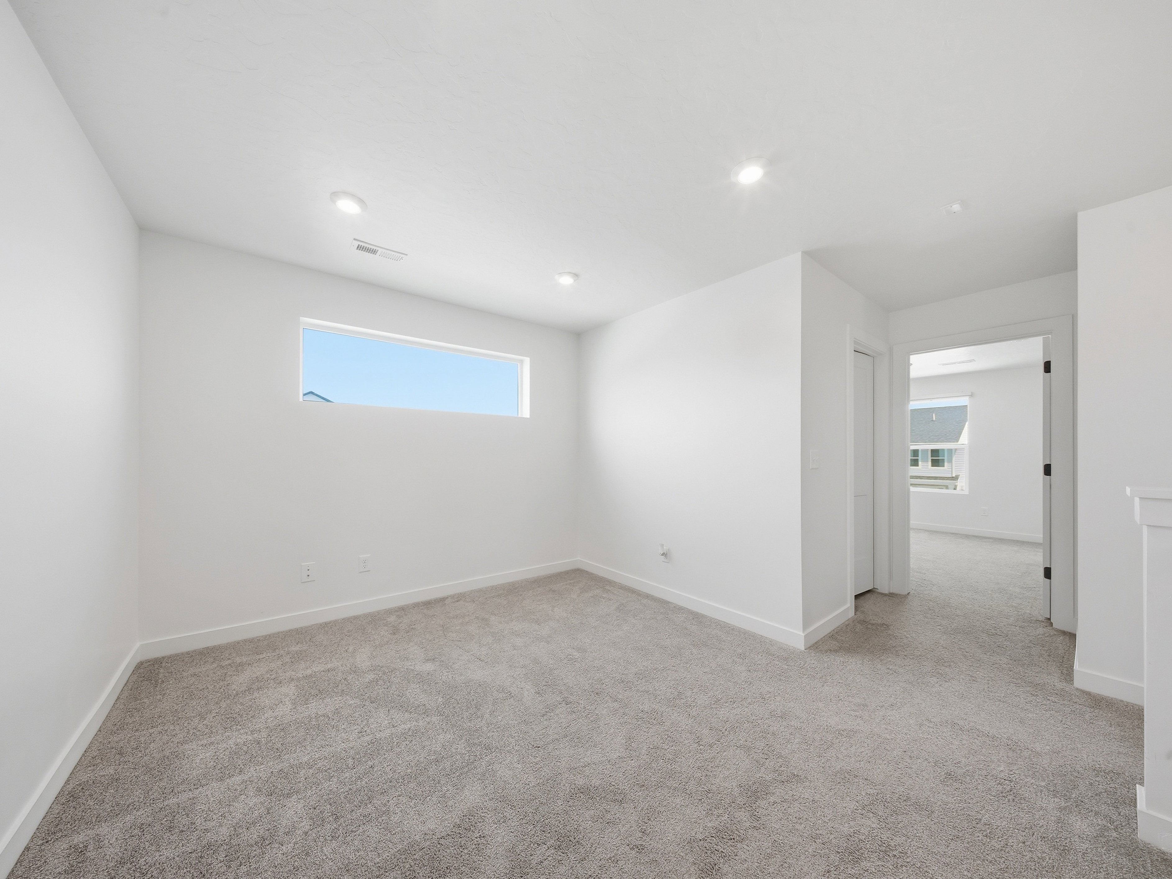 Spacious room featuring a horizontal window, recessed lighting, neutral carpeting, white baseboards, and a doorway to an additional room