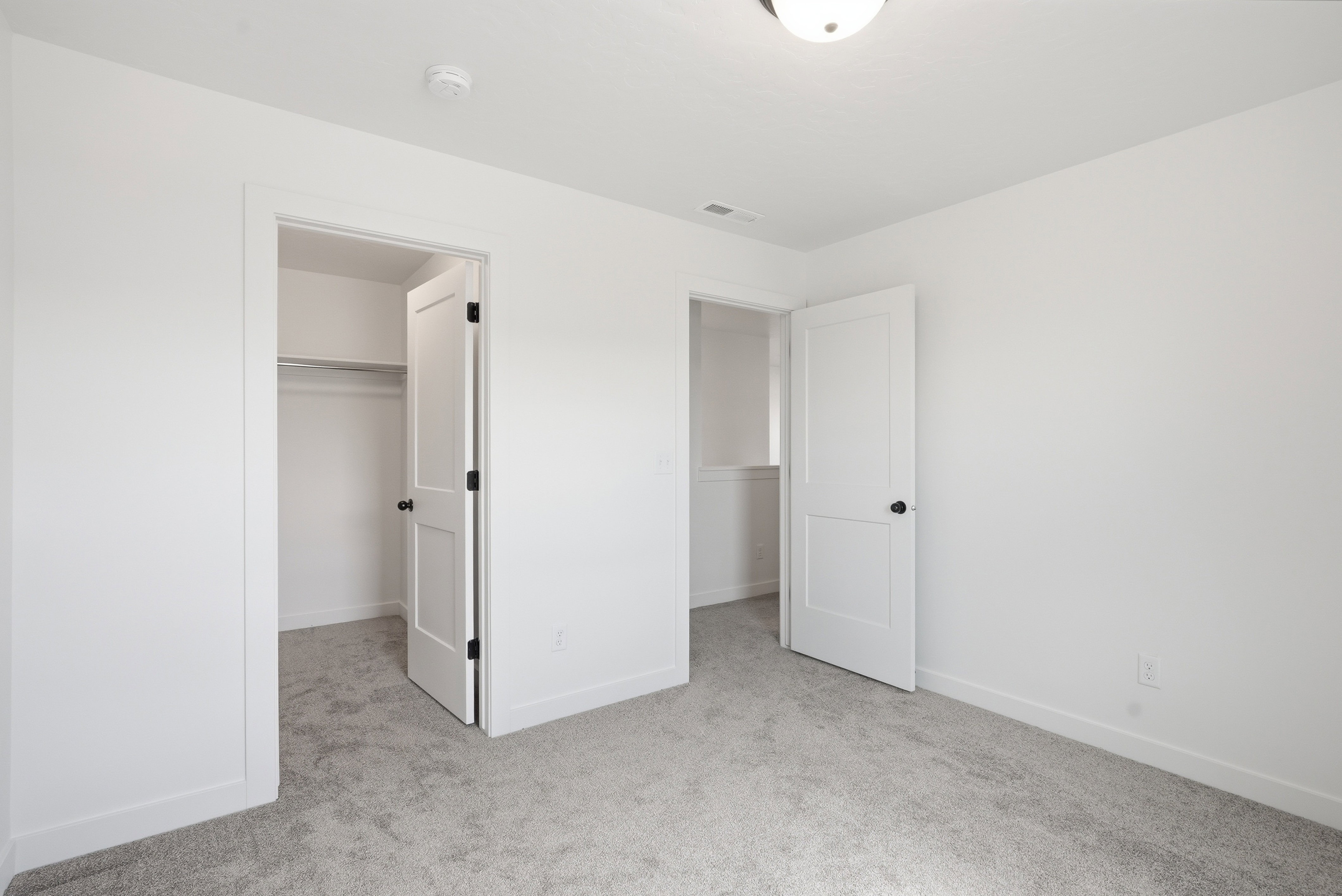 Neutral tone room featuring light gray carpeting, crisp white walls, white baseboards, and a semi-flush ceiling light fixture