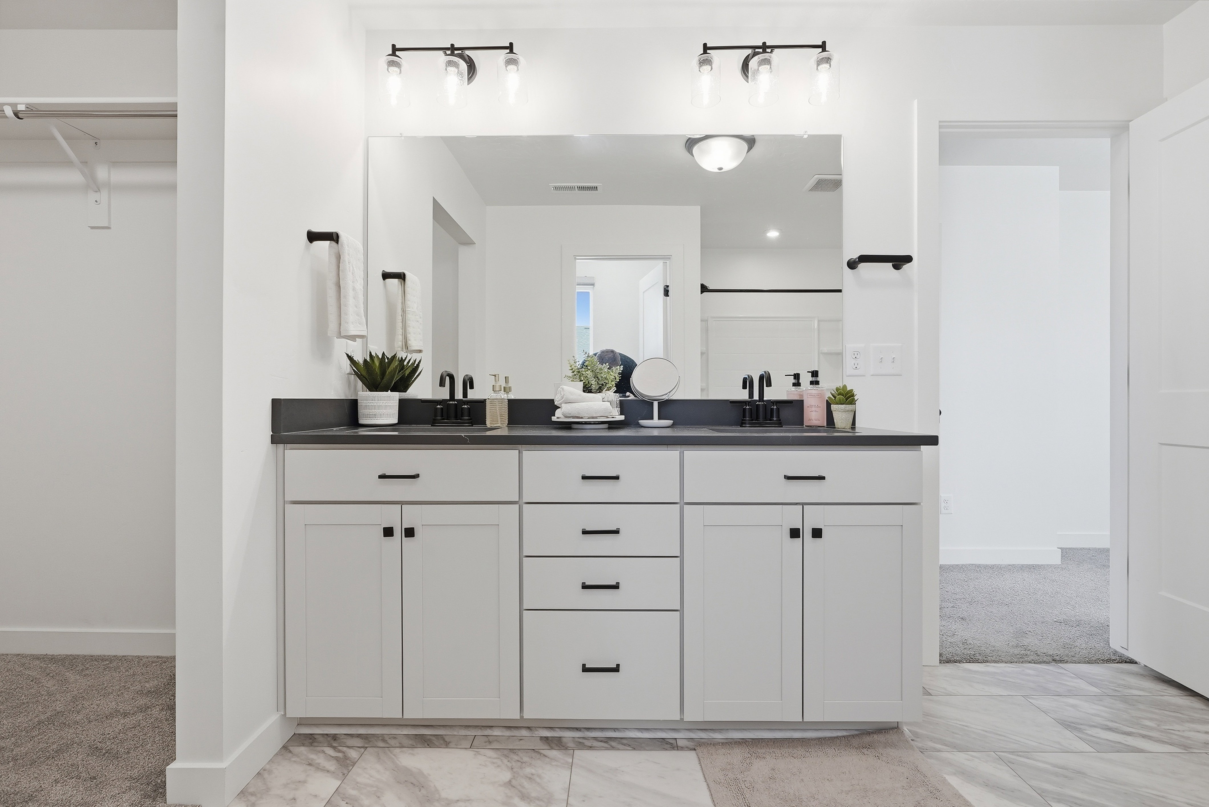 Dual vanity with black countertops, integrated sinks, white cabinetry, and matte black hardware