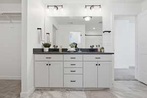 Dual vanity with black countertops, integrated sinks, white cabinetry, and matte black hardware