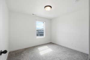 Bright interior space featuring a single window, overhead flush mount lighting, light gray carpeting, crisp white walls, and a visible electrical outlet
