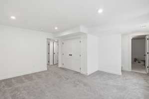 Spacious room featuring light gray carpet flooring, recessed lighting, white walls, and multiple paneled doors with black hardware