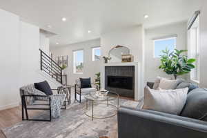 Bright living area featuring a tiled fireplace with white mantel, recessed lighting, wood-finish flooring, and a contemporary staircase with black railings