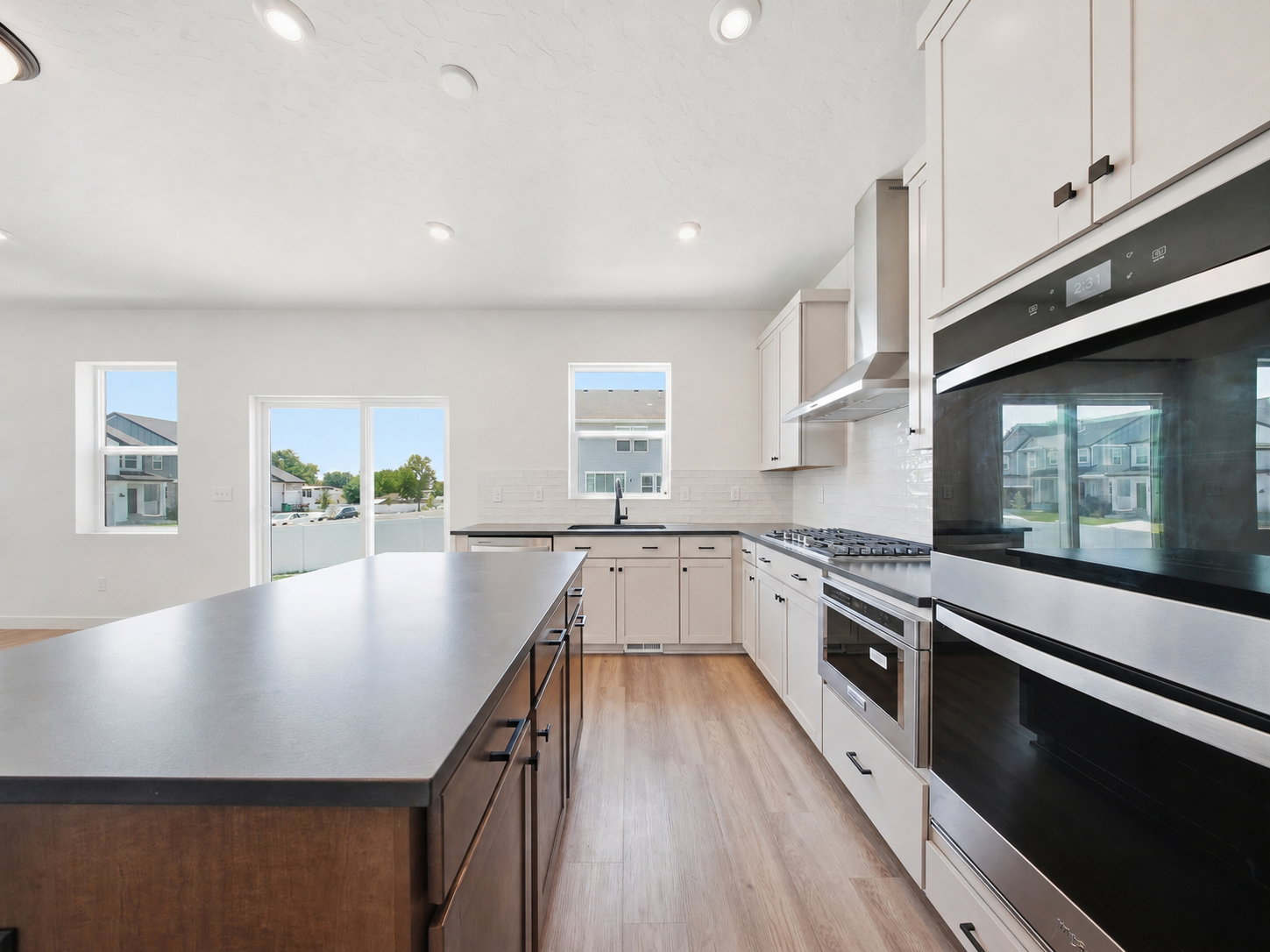 Kitchen featuring a large island with a dark countertop, light wood-finish flooring, white cabinetry, integrated stainless steel appliances, and a subway tile backsplash