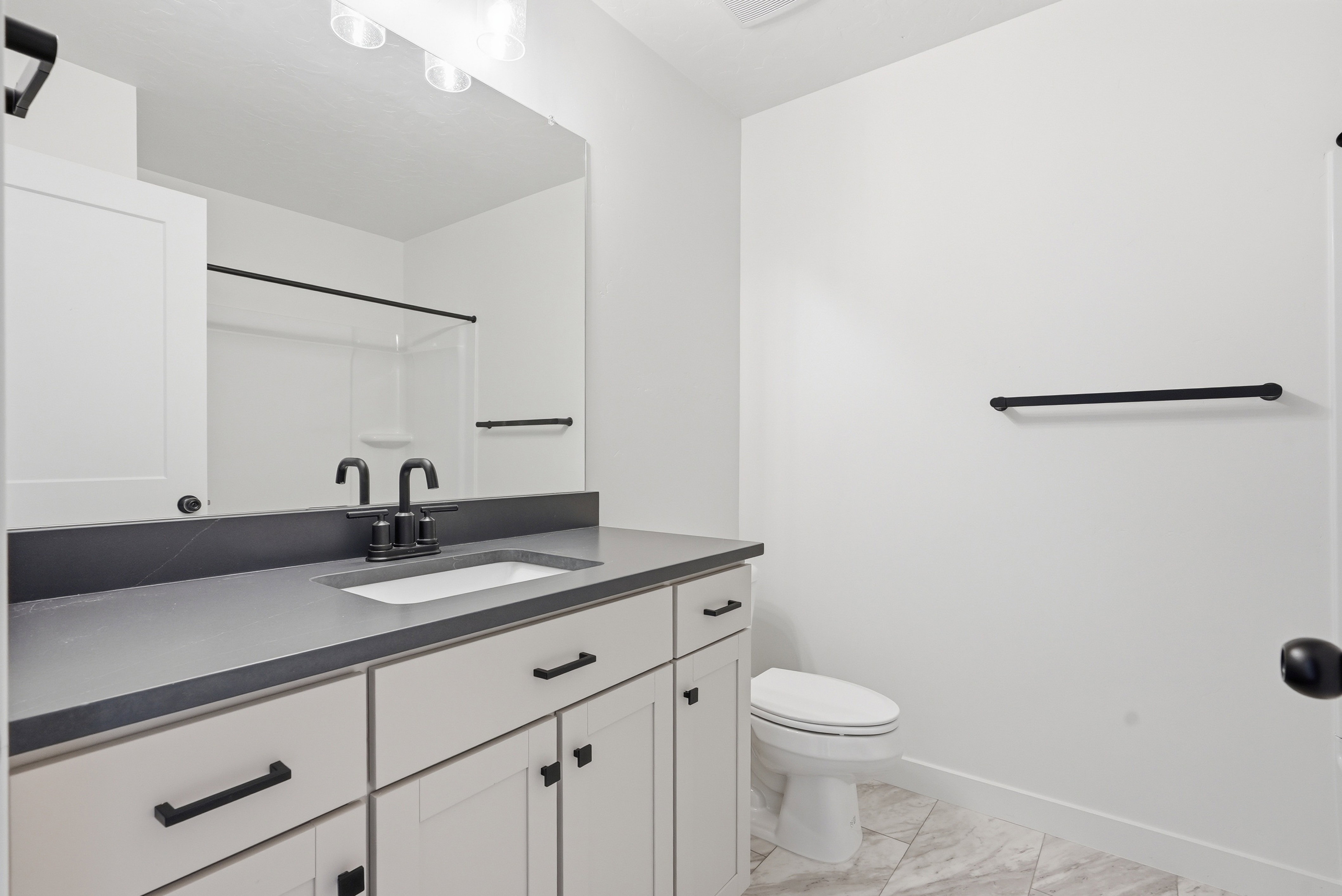 Bathroom featuring a single vanity with shaker-style cabinetry, matte black hardware, a grey countertop, and an integrated sink basin