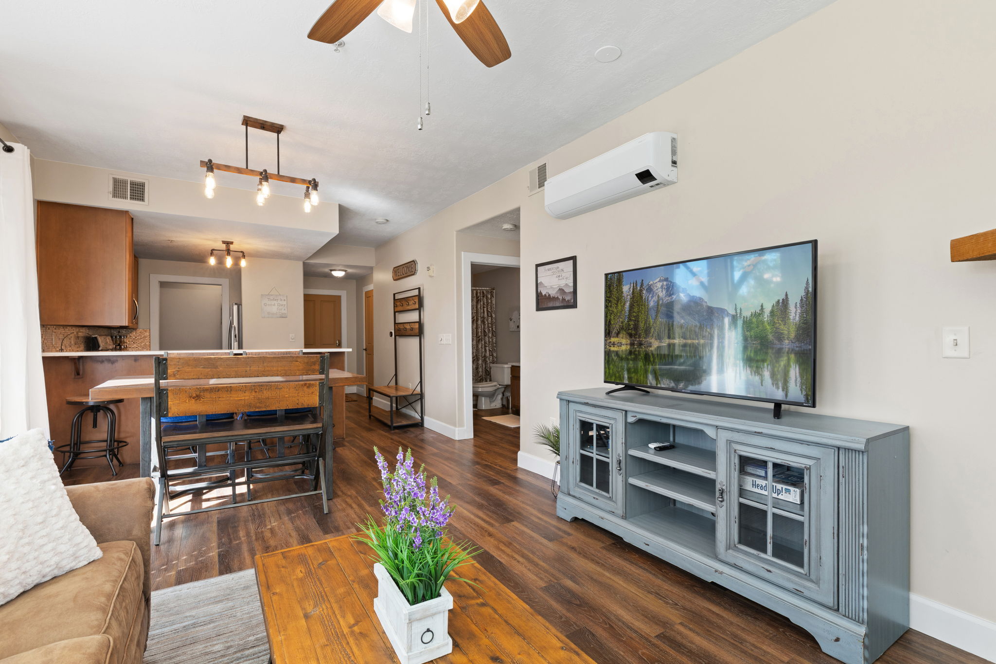 Open-concept living area featuring wood-finish flooring, a ceiling fan, and a wall-mounted mini-split system