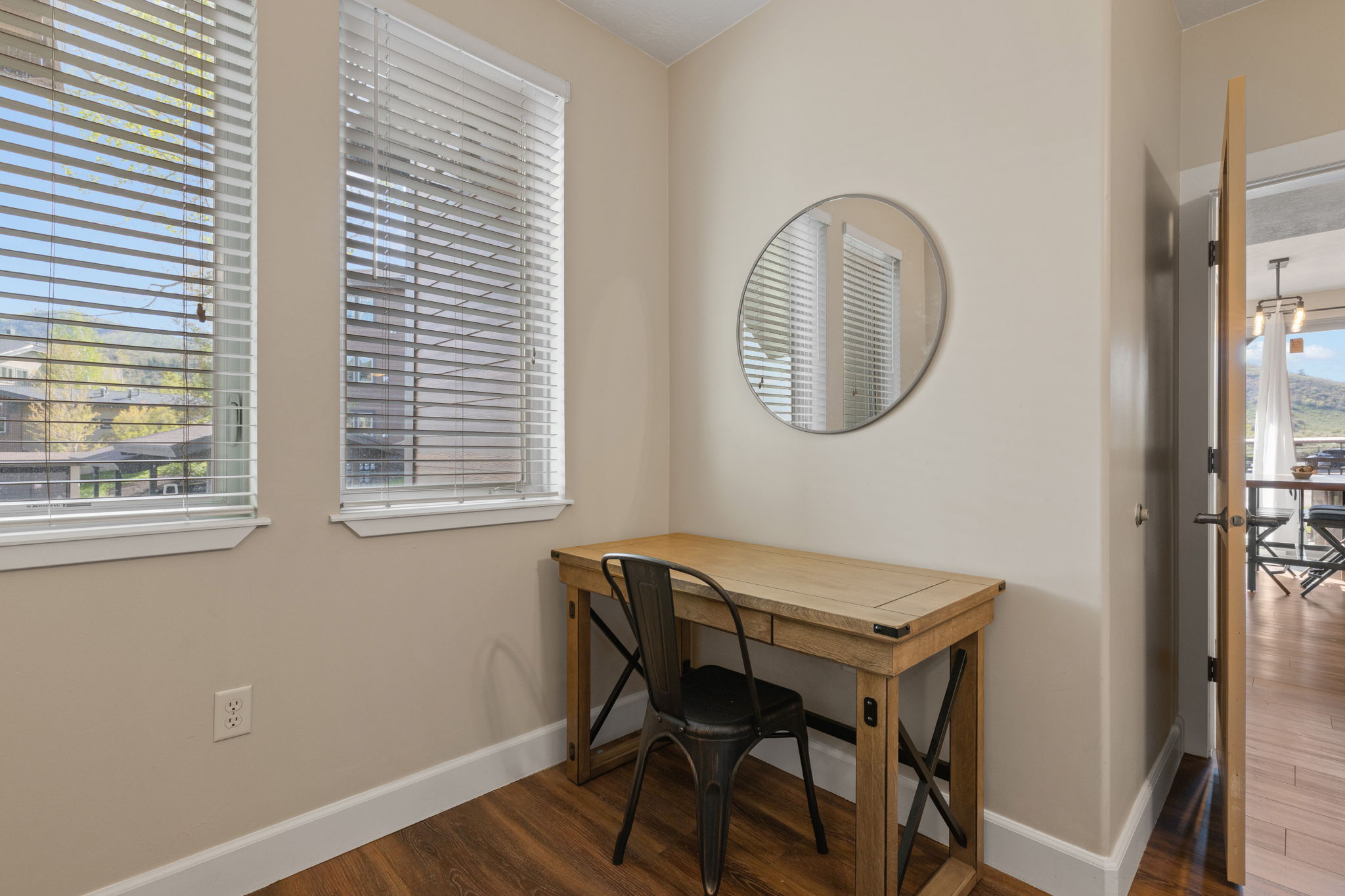 Dedicated workspace featuring two windows with horizontal blinds, wood-finish flooring, and a neutral wall color