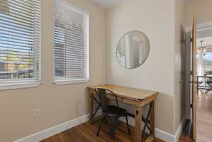 Dedicated workspace featuring two windows with horizontal blinds, wood-finish flooring, and a neutral wall color