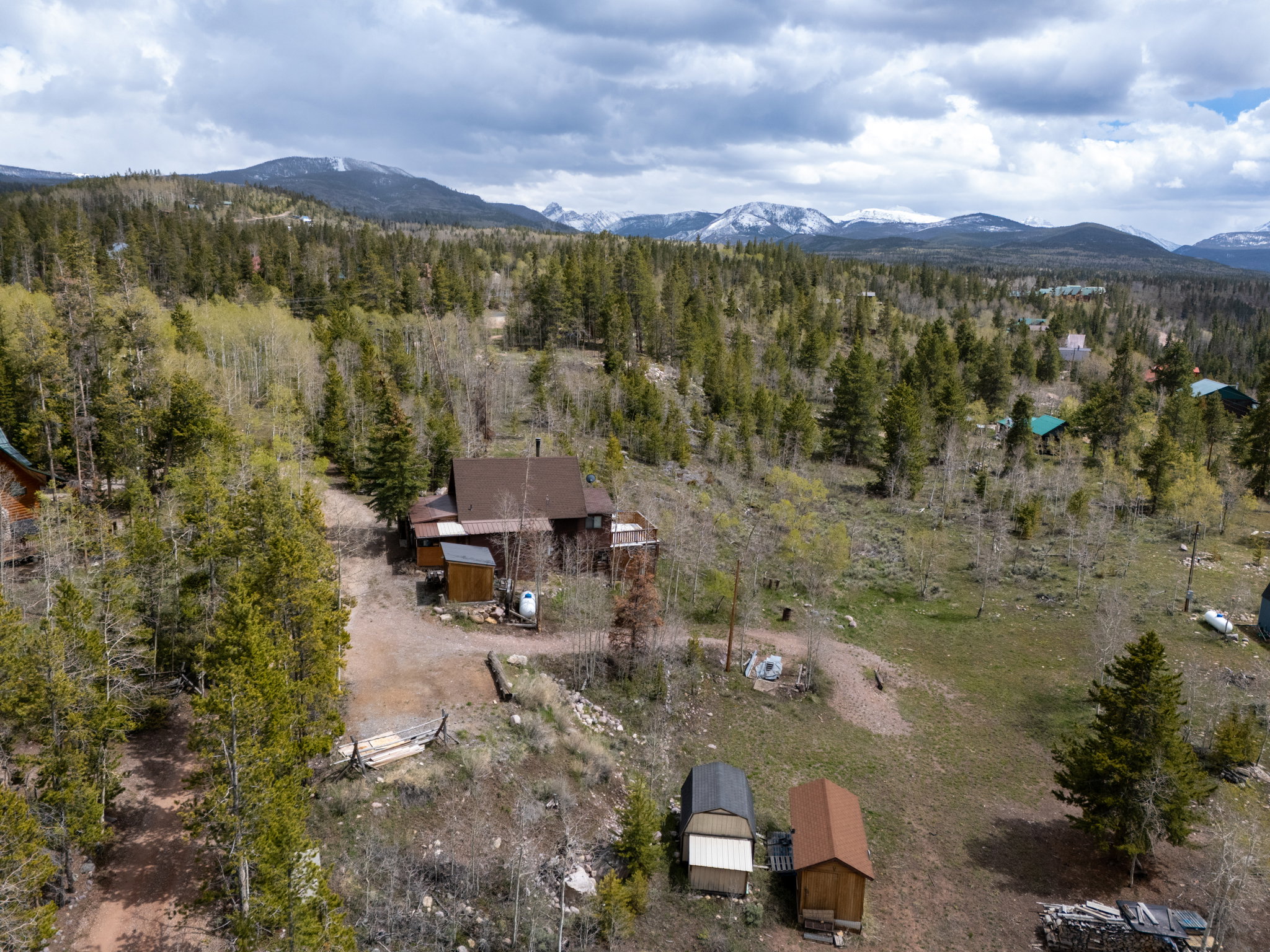 Mountain property surrounded by mature trees, featuring a multi-story residence with a brown roof and a detached shed