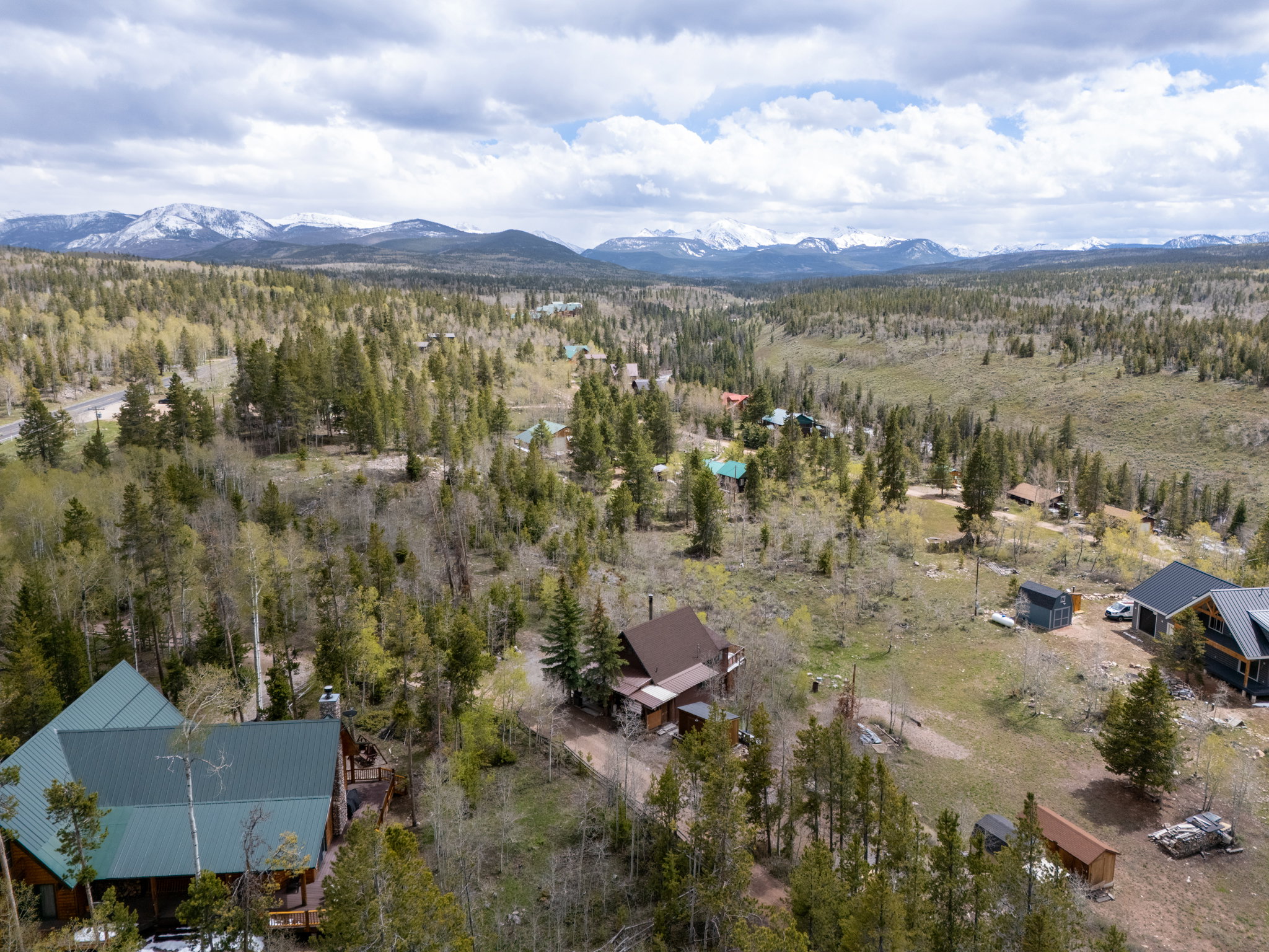 Expansive wooded landscape featuring mature trees, distant snow-capped mountains, and a clear sky with scattered clouds