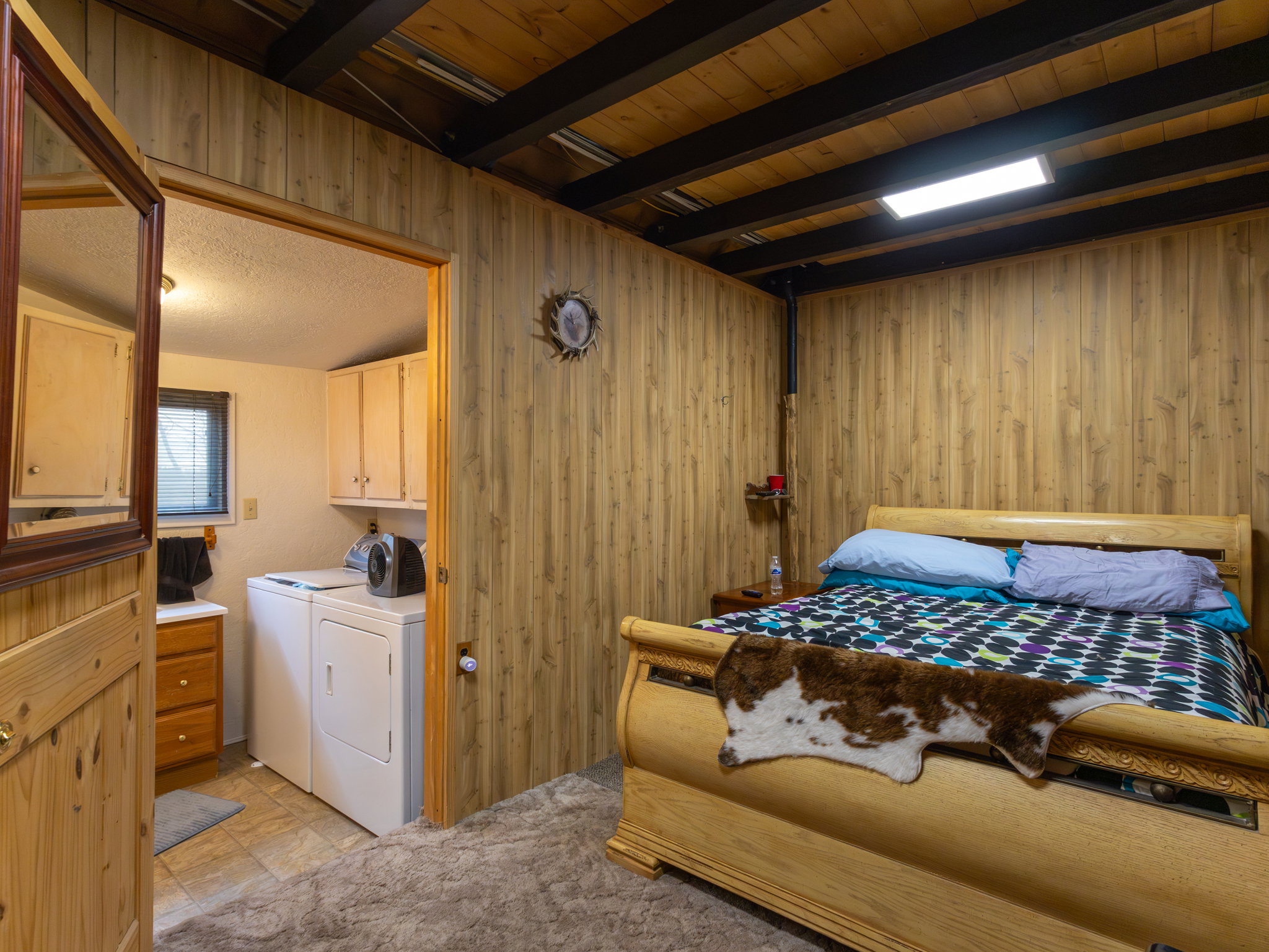 Room featuring natural wood paneling, exposed ceiling beams, and a light wood bed frame