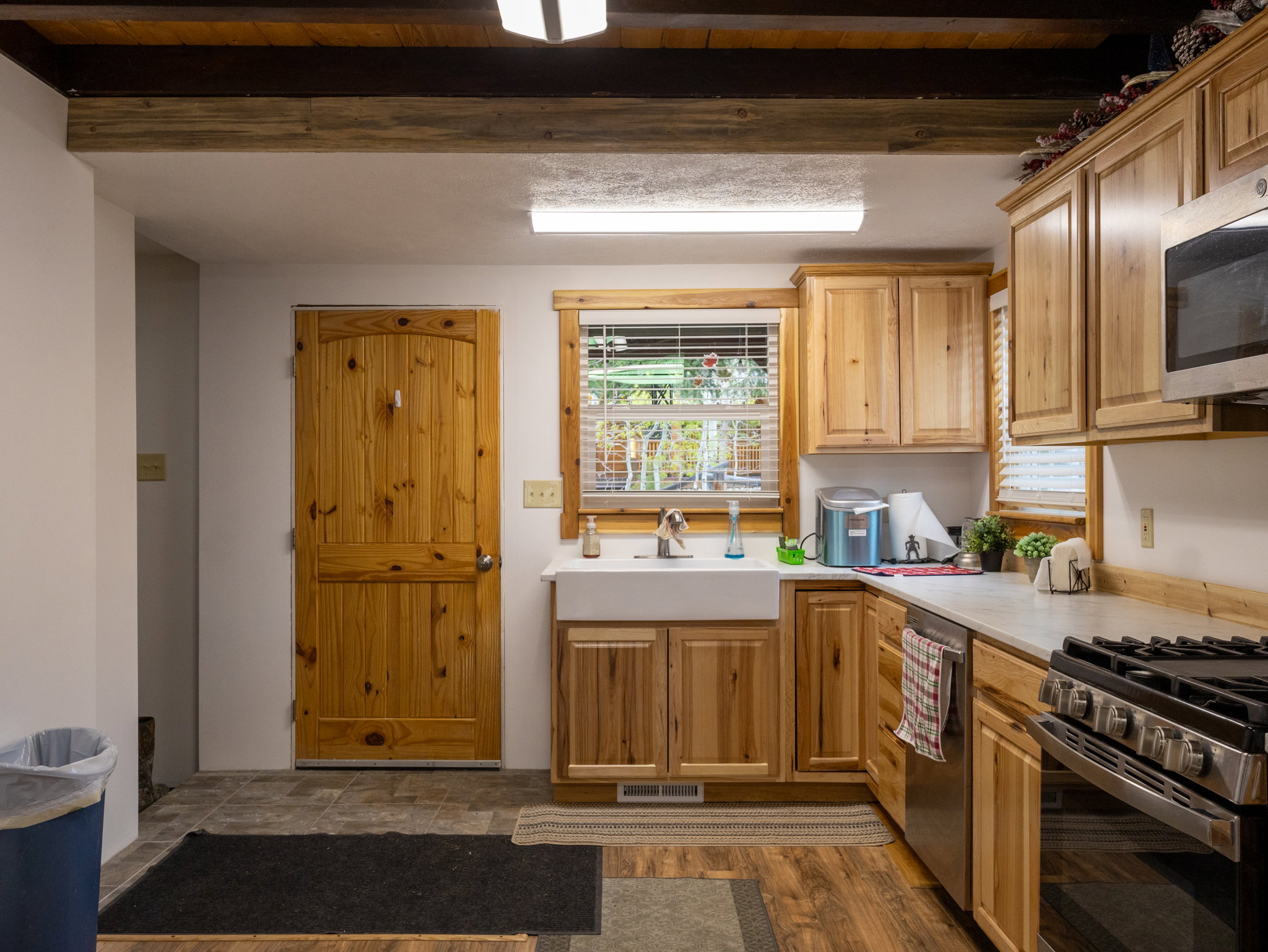 Kitchen featuring natural wood cabinetry, a farmhouse sink, stainless steel appliances, and wood-finish flooring